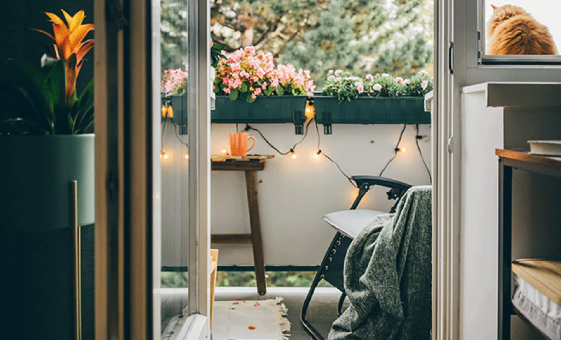 Sicht auf einen mit Lichterketten, Kuscheldecken und Blumenkästen geschmückten Balkon.