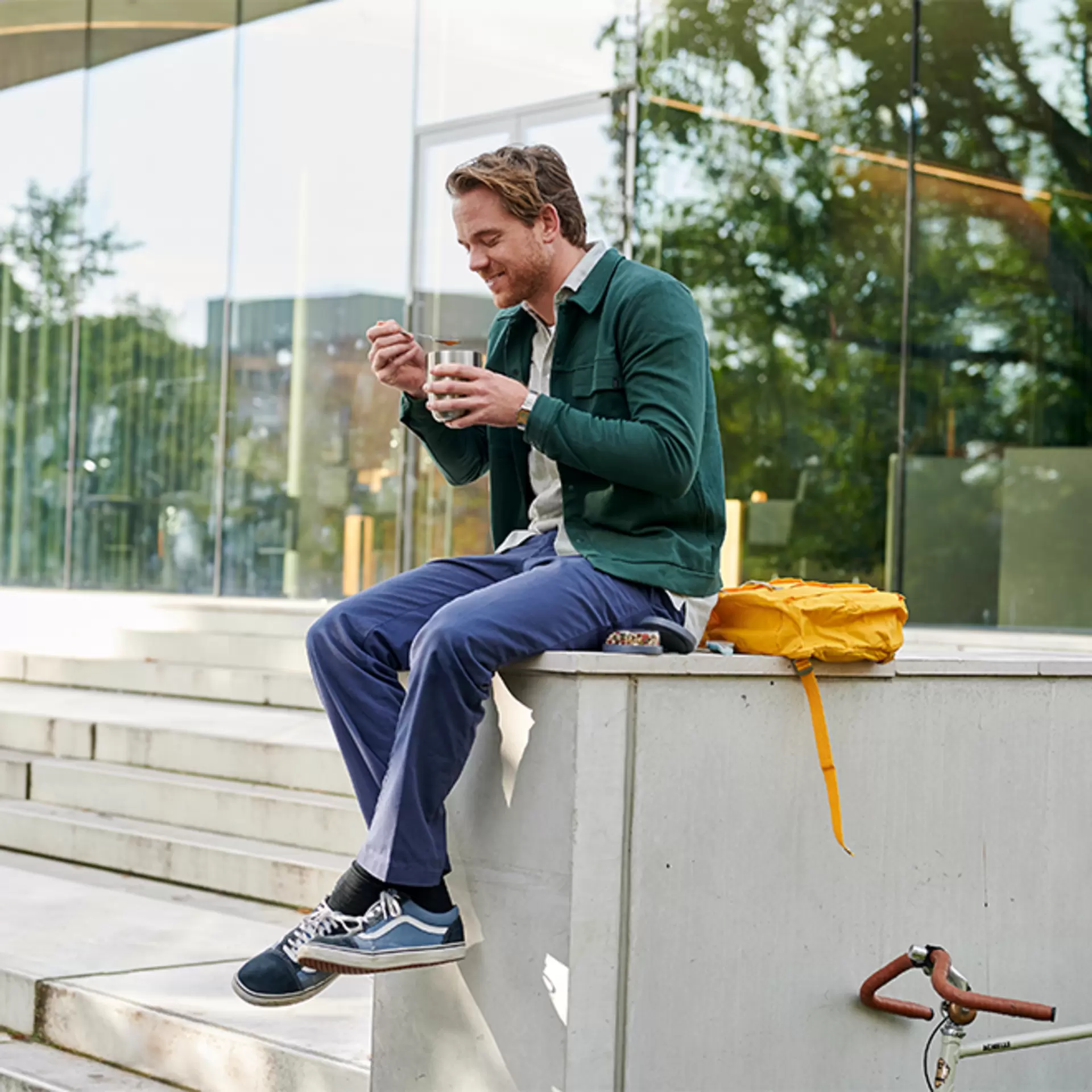 Ein Mann sitzt auf einer Mauer und Isst aus seinem Mepal Thermobecher