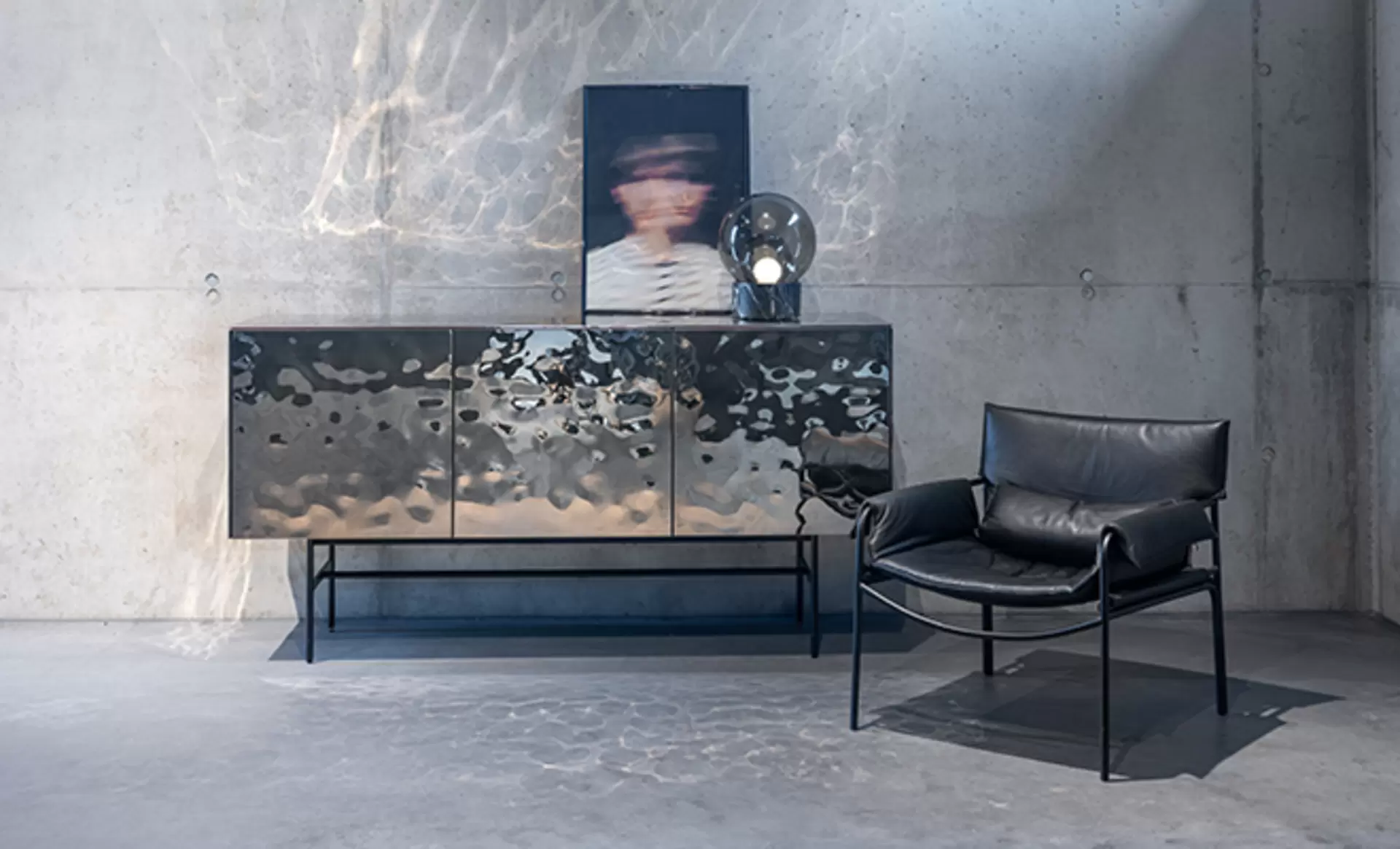 Ein Sideboard von Kettnaker aus der Serie Soma mit einer glänzenden hammer geschlagenen Oberfläche. Davor steht ein Leder Sitzstuhl