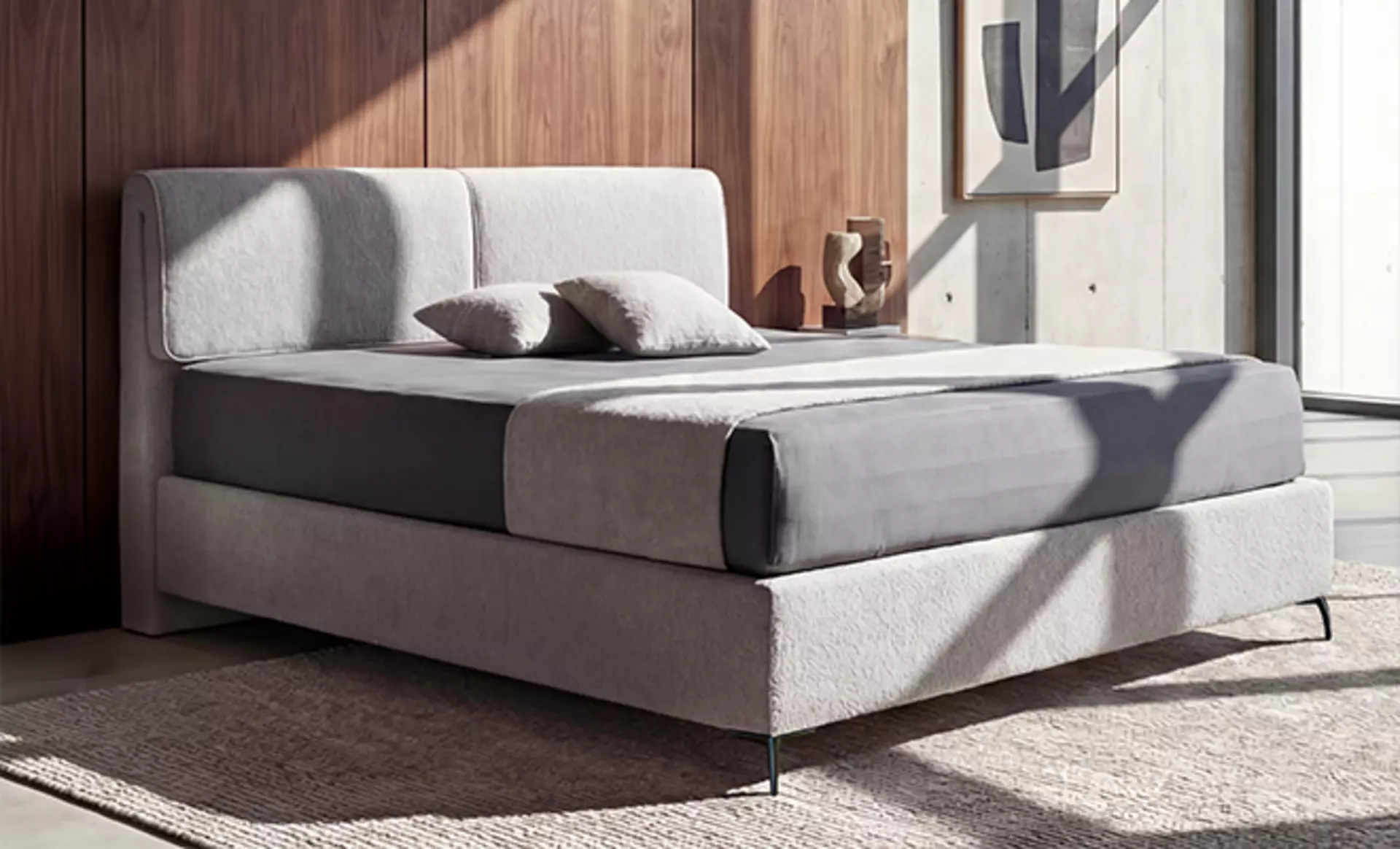 Das Hülsta Cuello Boxspringbett in grauem Stoffbezug in einem Lichtdurchfluteten Schlafzimmer