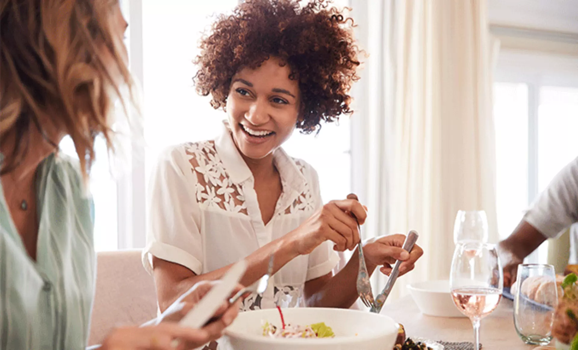 Eine Frau sitzt mit ihren Freunden am Esstisch und unterhält sich fröhlich beim Abendessen.