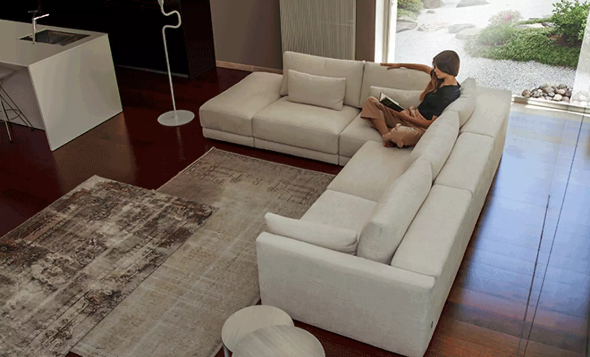 Frau sitzt entspannt auf einem großen weißen Sofa von Calia Italia und liest ein Buch.