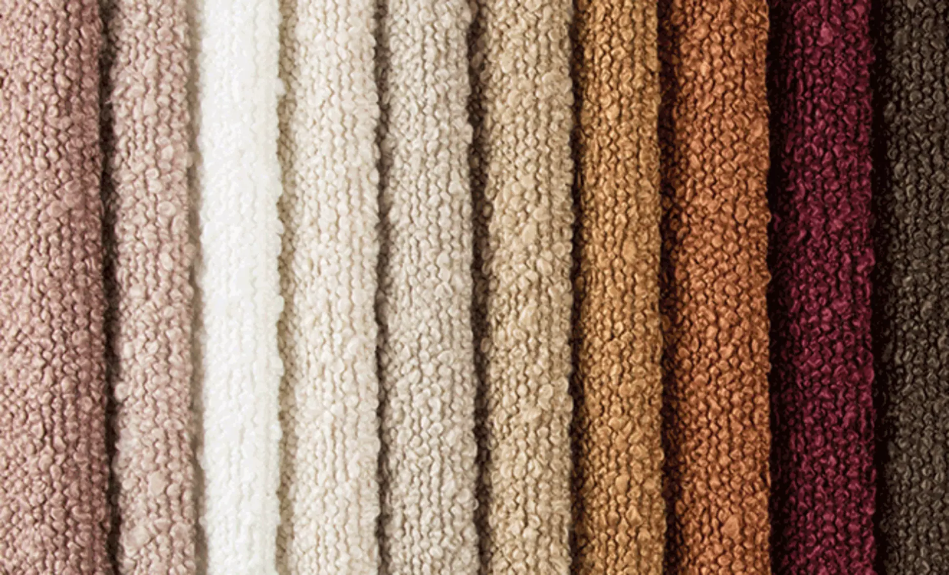 Verschiedene Bouclé-Stoffe in hellen Naturtönen als Materialtrend für ein frühlingshaftes Wohnzimmer.