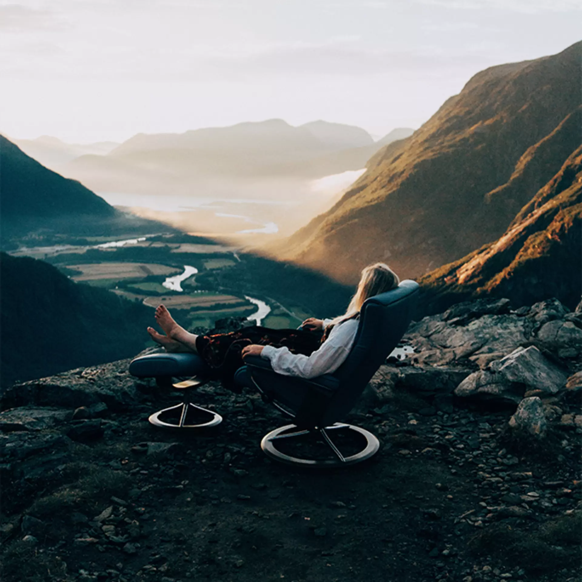Eine Frau sitzt in einem Stresssless Relaxsessel mit Fußsteil auf einer Klippe in den Norwegischen Bergen und Blickt in die Ferne