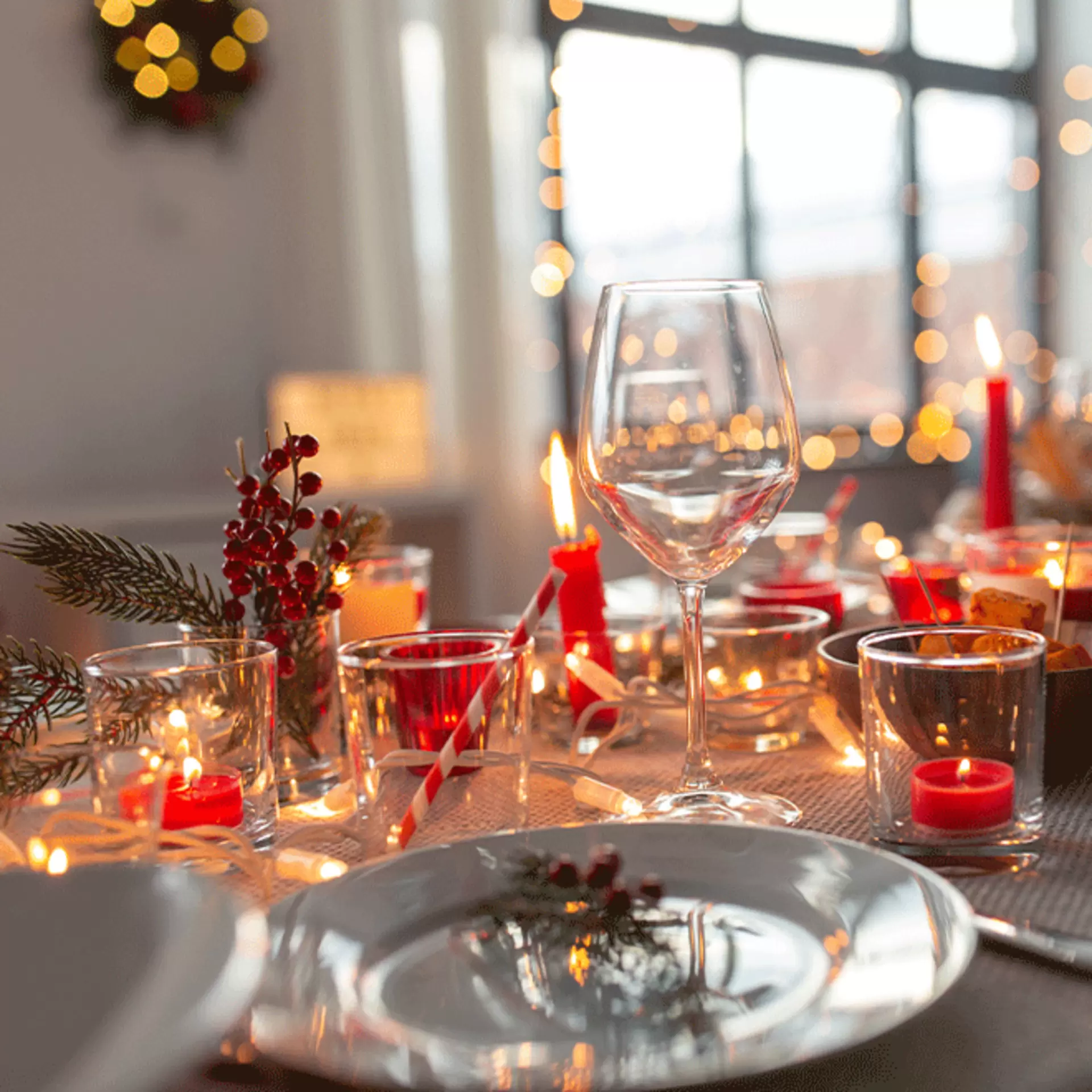 Festive Tischdekoration mit vielen brennenden Kerzen, Teelichtern im Glas, Lichterkette und funkelnden Weingläsern auf der Tafel