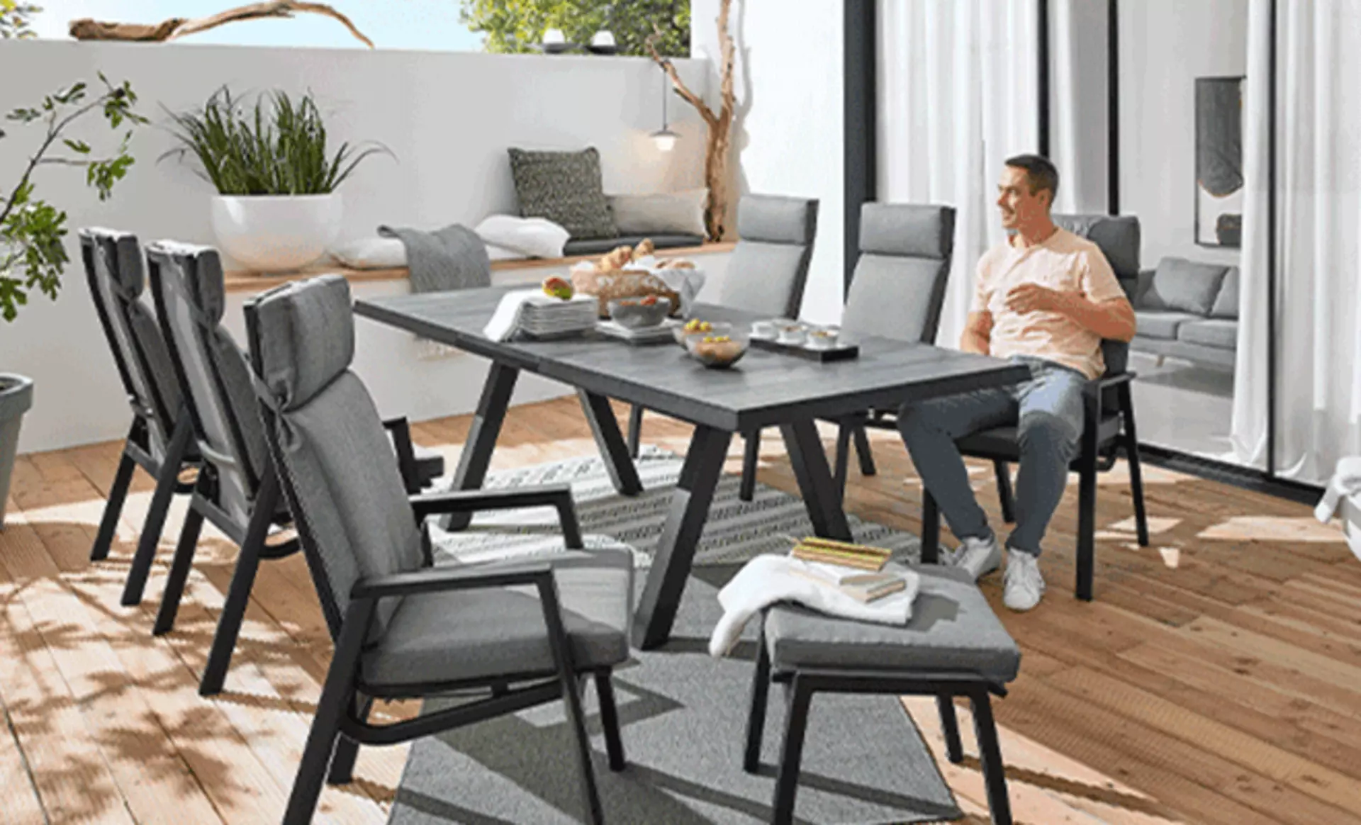 Ein Mann Entspannt an einem grauen Gartentisch mit passenden Stühlen