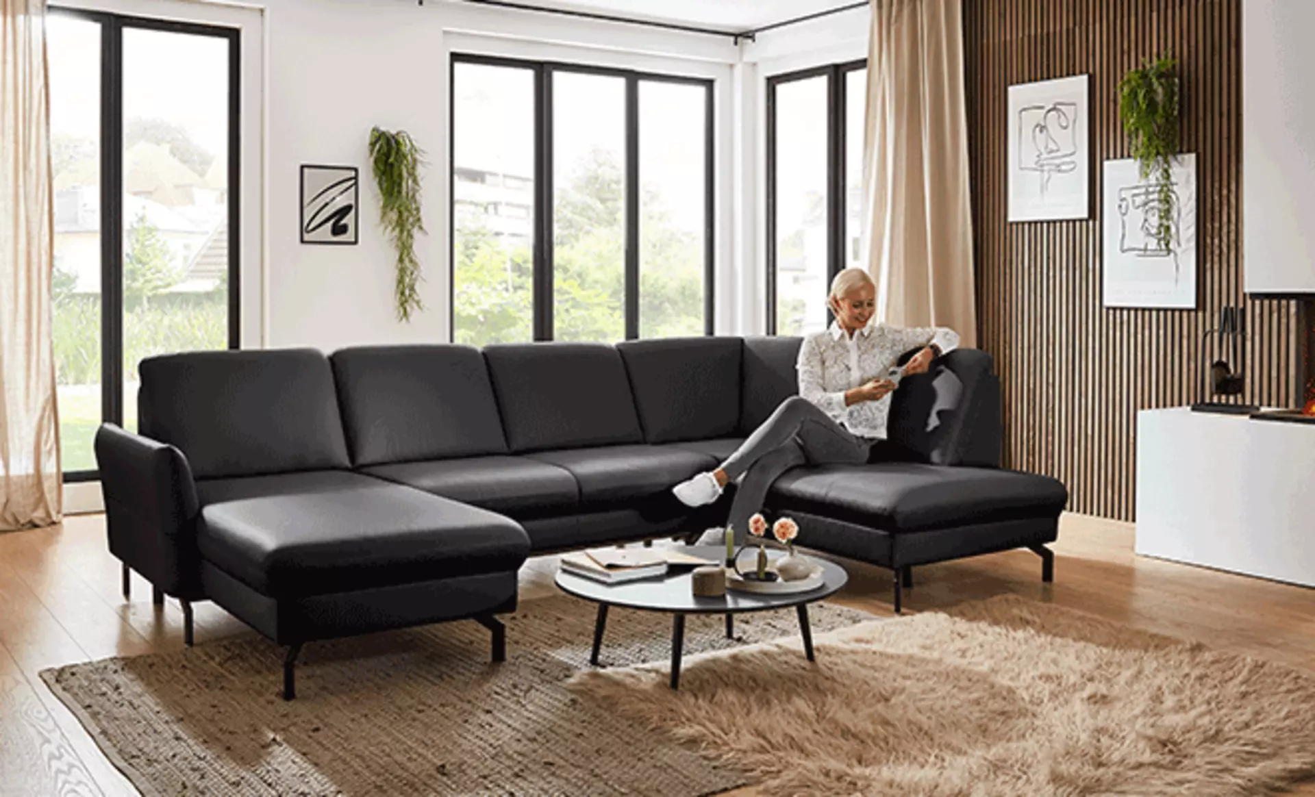 Schwarzer Ecksofa wo eine Frau drauf sitzt 