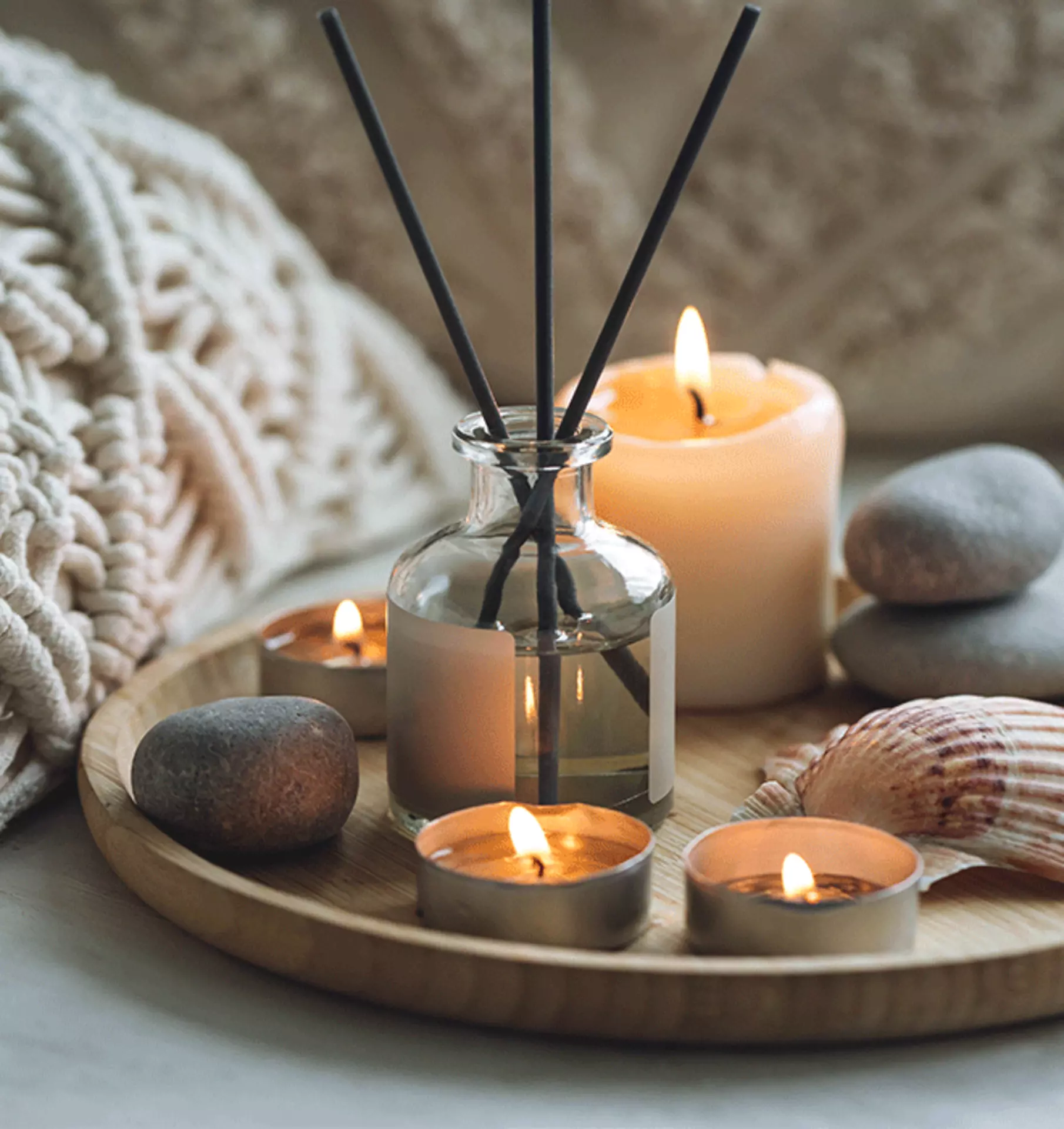 Raumduftflasche auf einem Tablett, umgeben von brennenden Kerzen – stimmungsvolle, gemütliche Dekoration