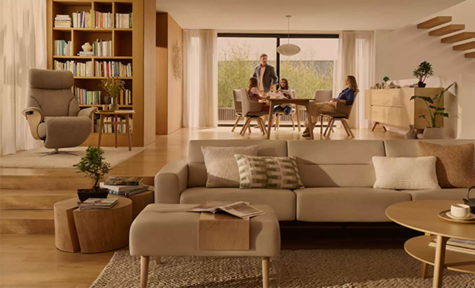 Offener Wohn-Essbereich mit einer Familie am Esstisch. Eine Wohonlandschaft und Relaxsessel von Stressless sind im Vordergrund zu sehen.