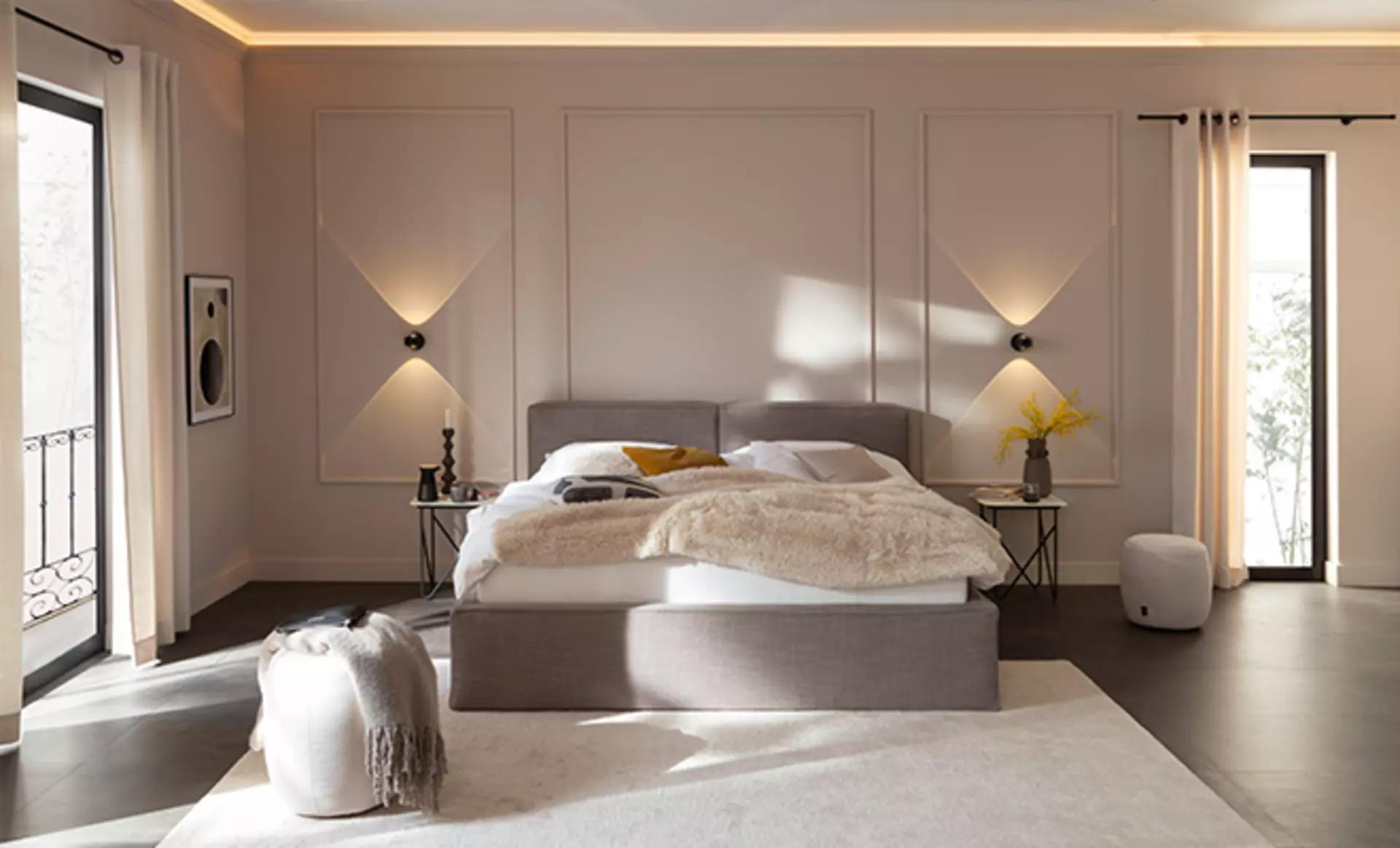 Das Vita Bett der Schöner Wohnen Kollektion in grauem Stoffbezug. Fotografiert in einem offenen Schlafbereich mit Wandleuchten am Kopfteil und passiver Deckenbeleuchtung
