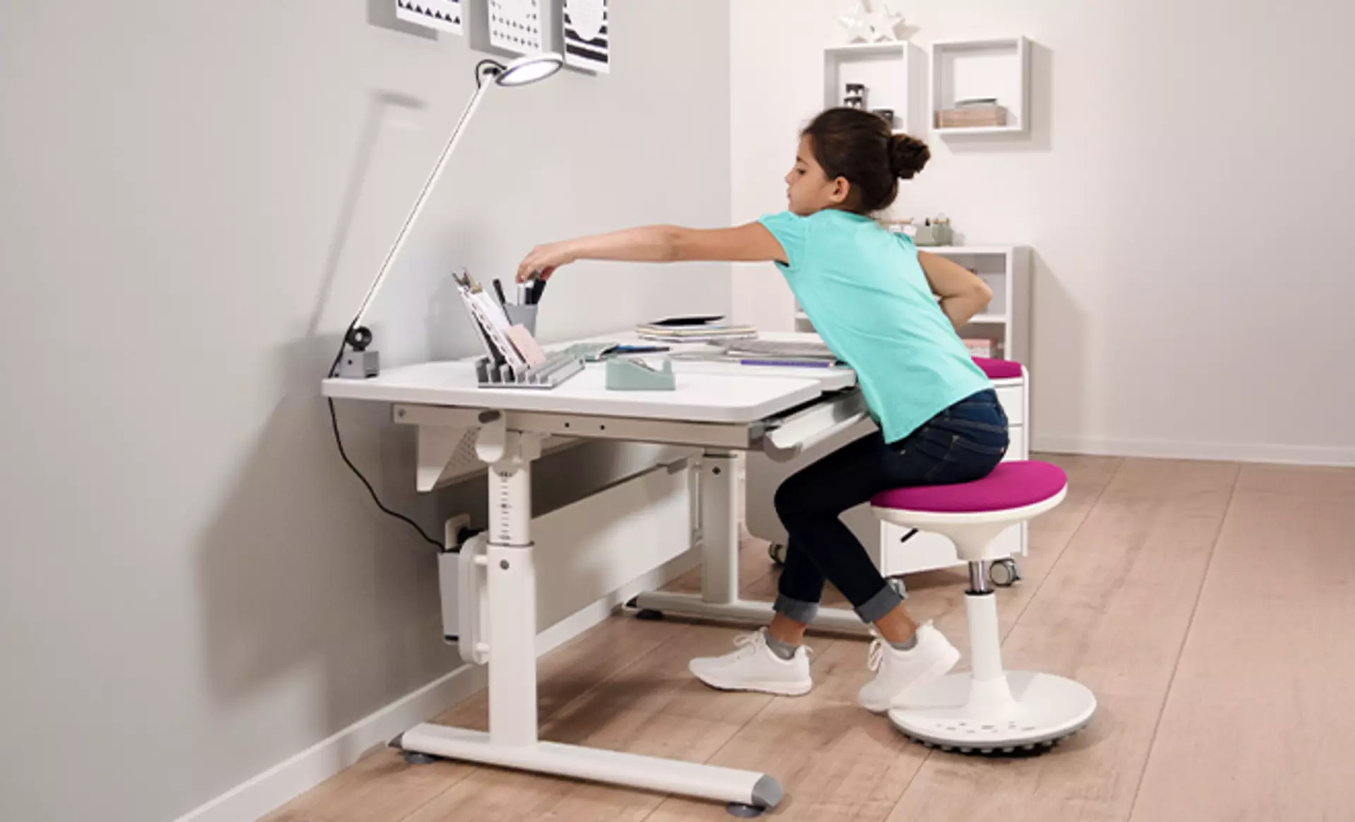 Mädchen Sitzt an einem Höhenverstellbaren Schreibtisch auf einem ergonomischen Hocker und bastelt