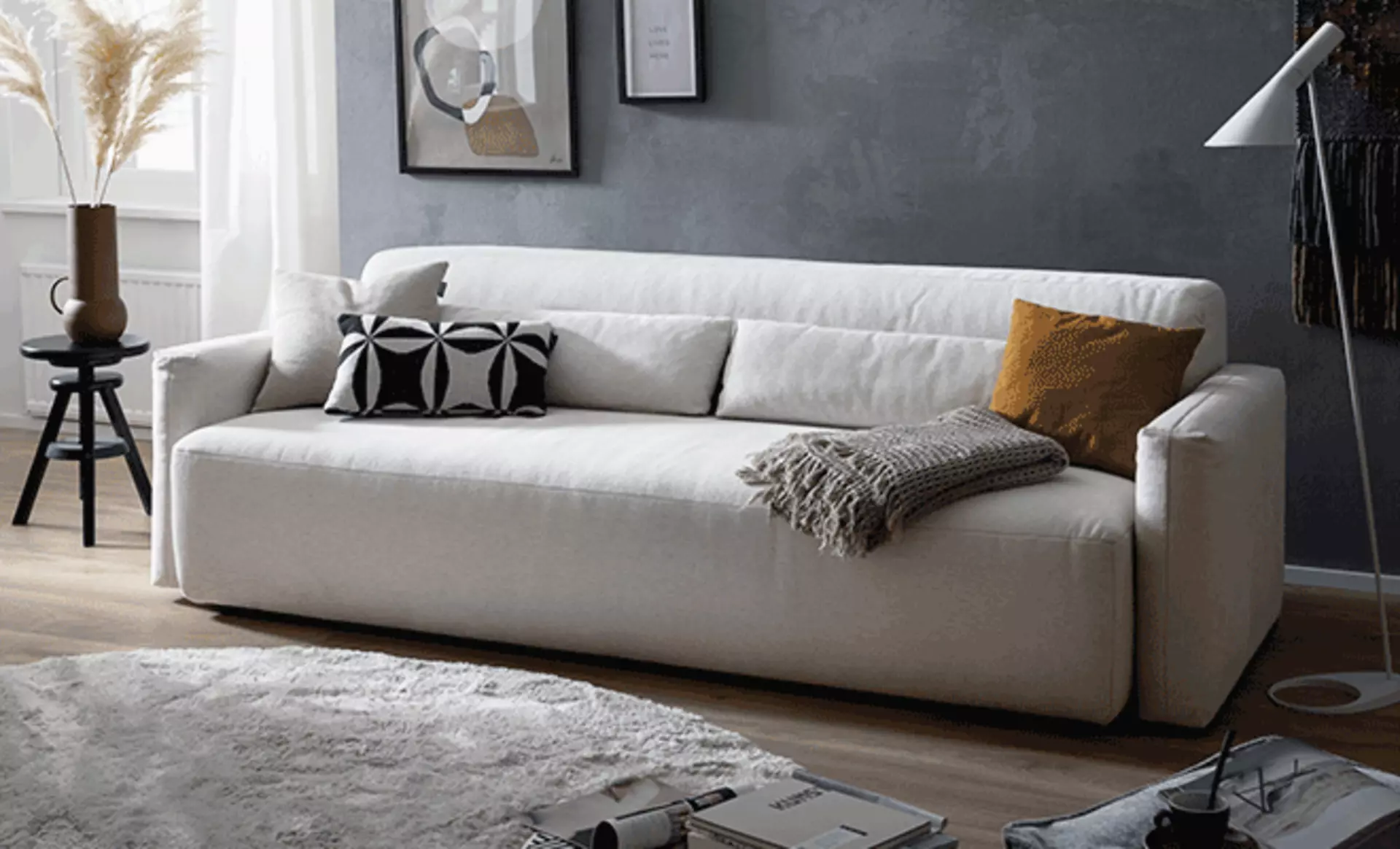 Weißer Schlafsofa das mit Kissen und einer Kuscheldecke dekoriert ist 