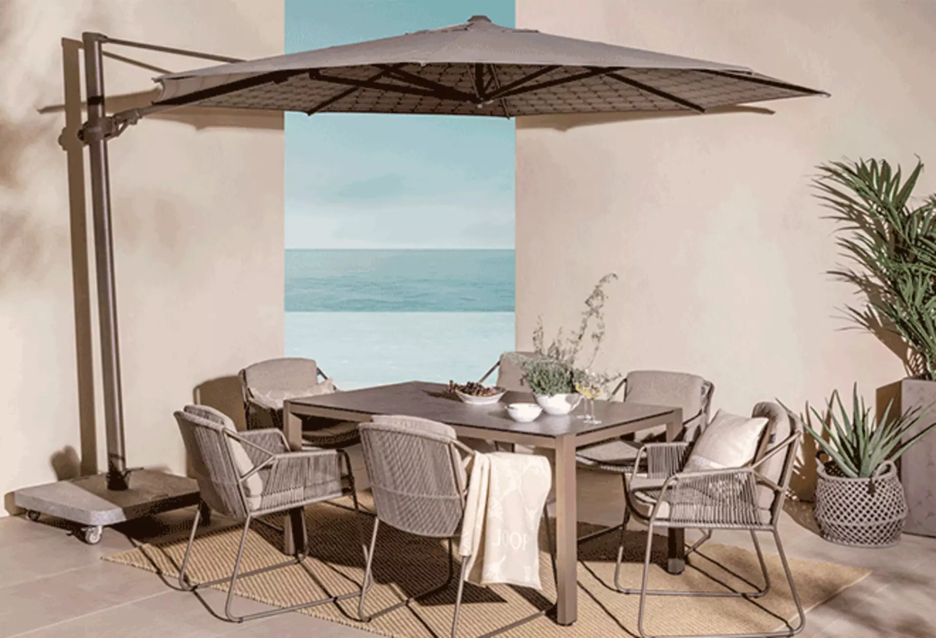 Grauer Ampelschirm über Essbereich mit Gartenmöbeln nahe am Meer.