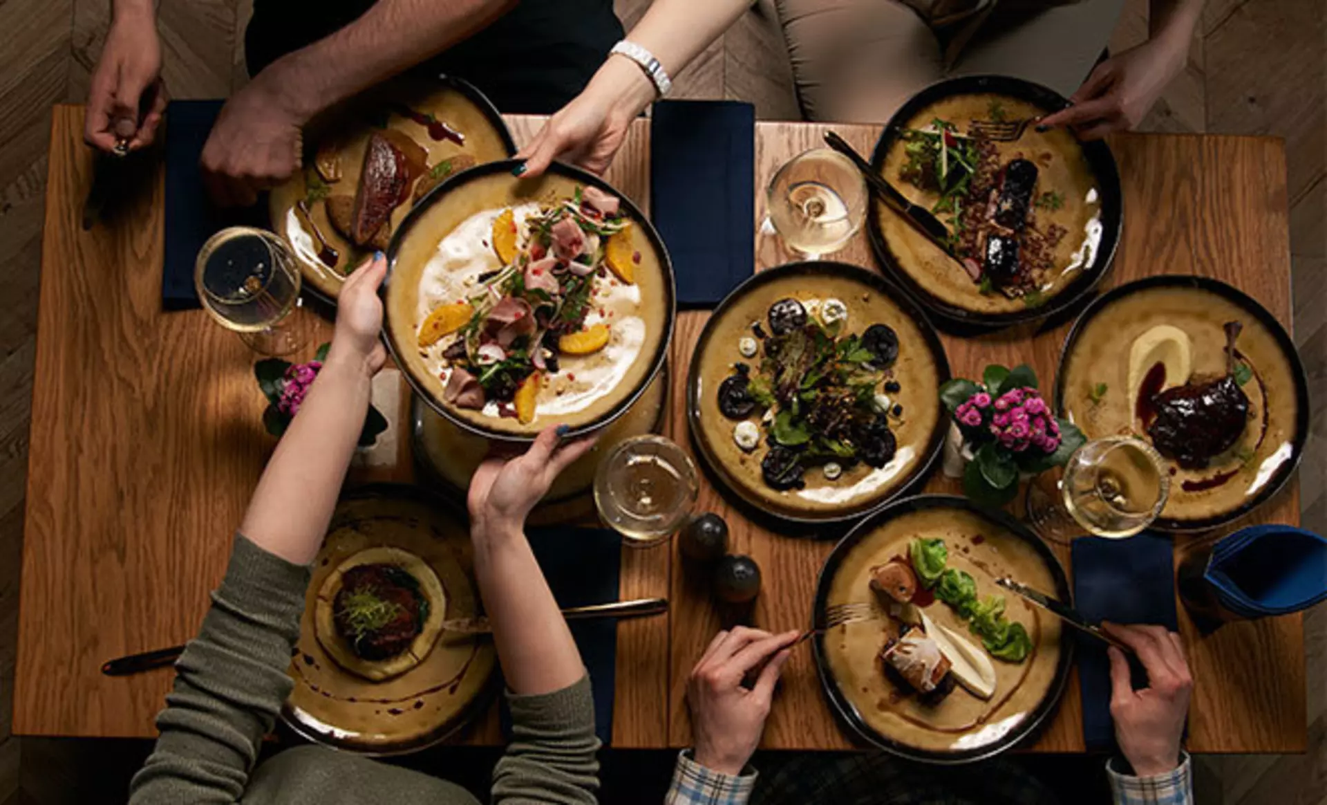 Esstisch aus Holz, dekoriert mit dunkelfarbigen Tellern, marineblauen Servietten und frischen Blumen, für eine Abendessenparty.
