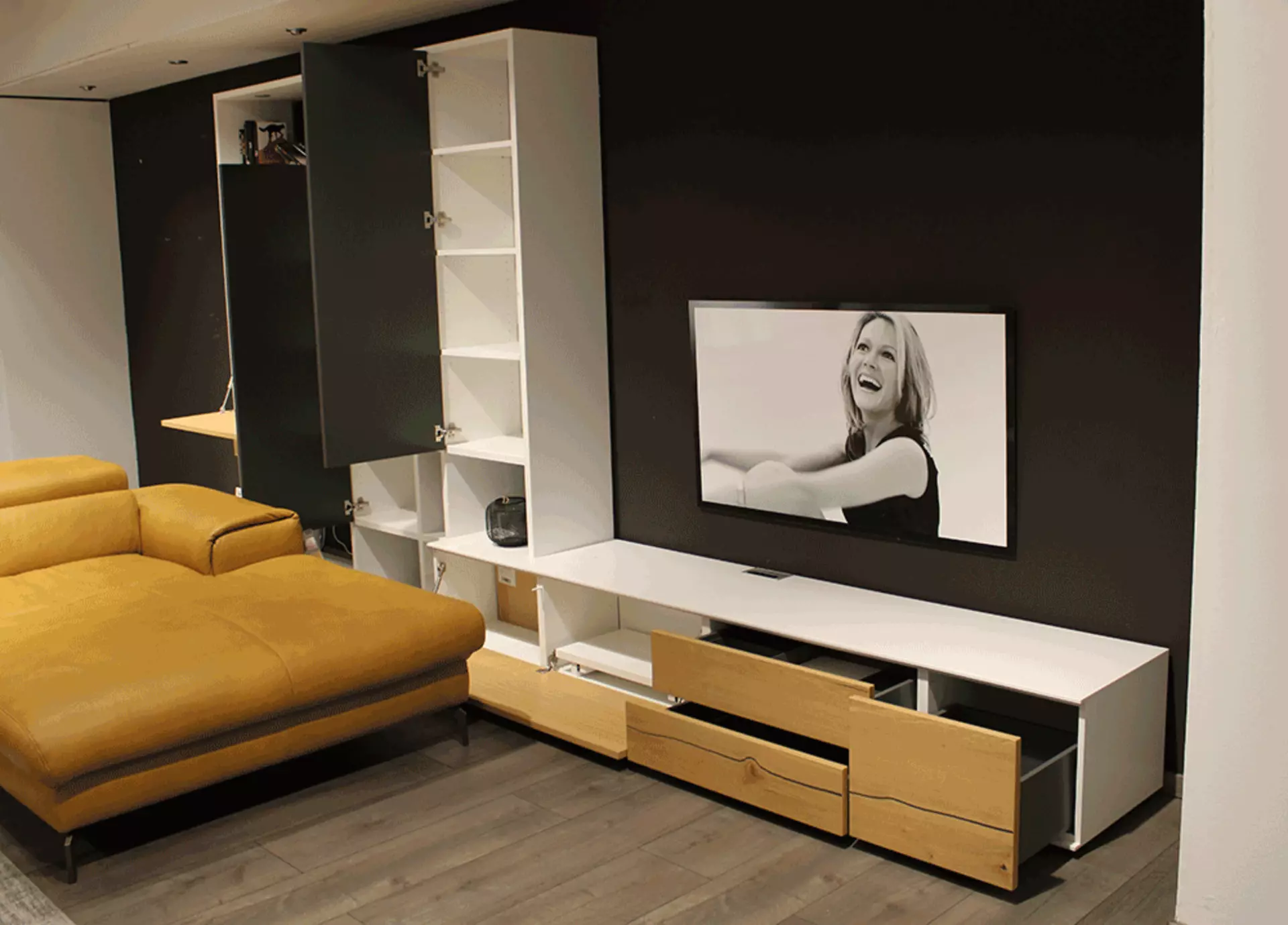 Eine Weiße Wohnwand ausgestatet mit Schubladen und Regalen deren Türen Offen sind und man eine Fläche sieht die extra für Fernseher sind