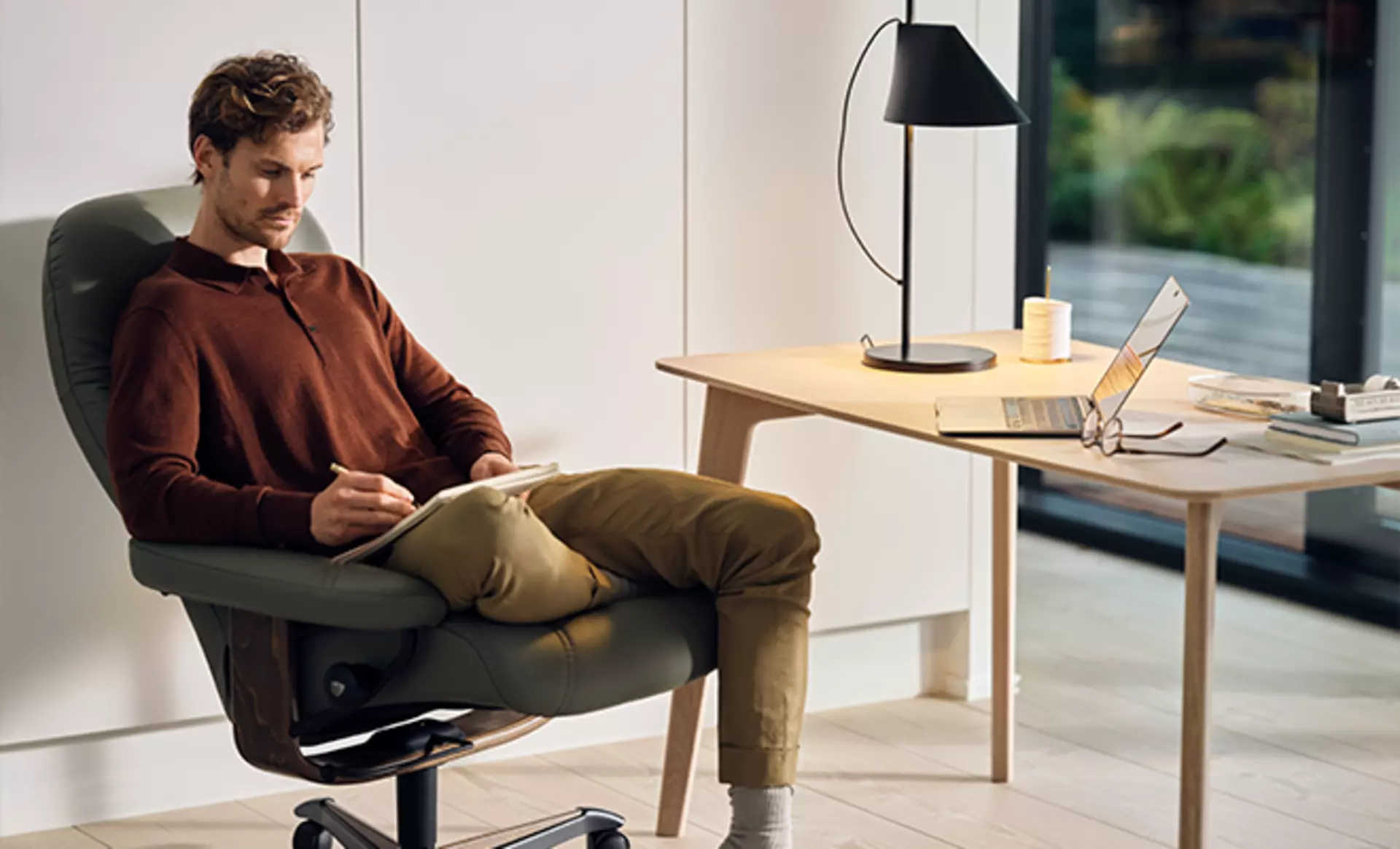 Ein Mann sitzt im Home Office in seinem Stressless Consul Bürostuhl gepolstert in Shadow Green Leder mit Walnuss Fußgestell
