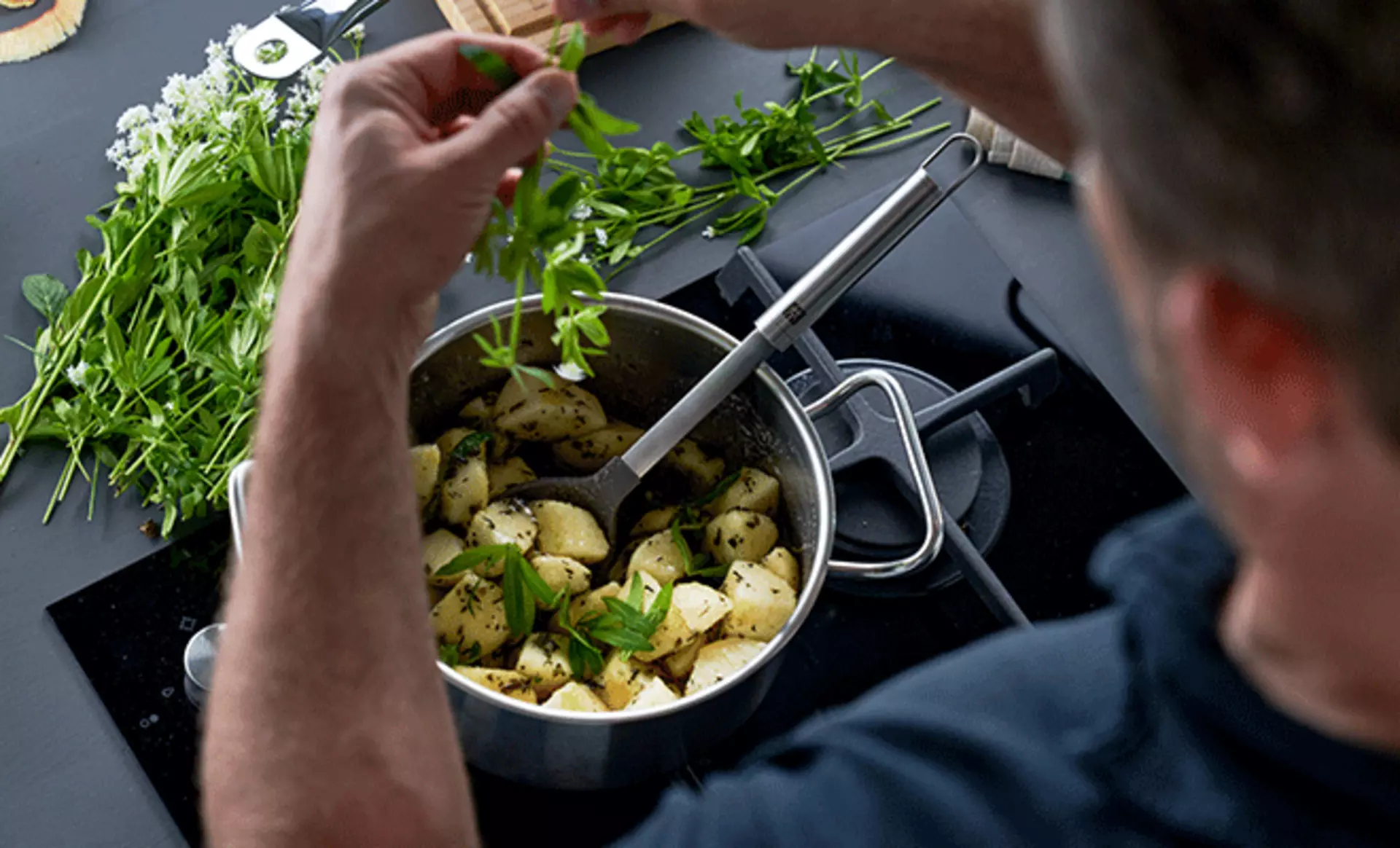 Ein Mann kocht mit einem hochwertigen Zwilling-Topf und gibt frische Kräuter hinzu.