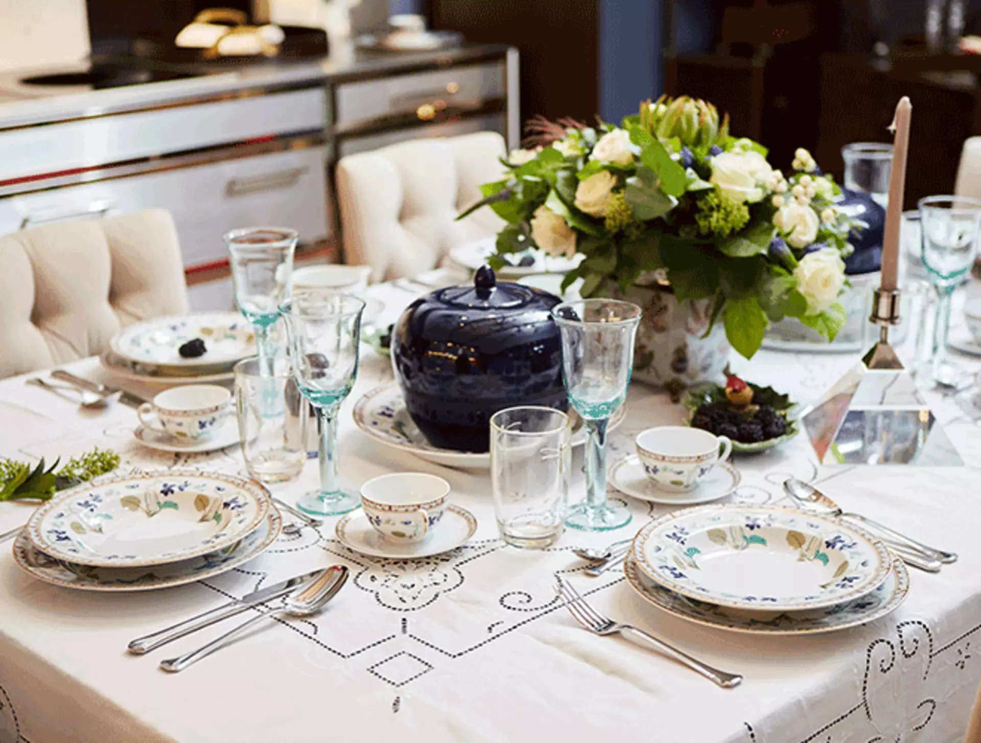 Esstisch mit weißen Blumen und weißen Tellern mit bunten Details dekoriert.