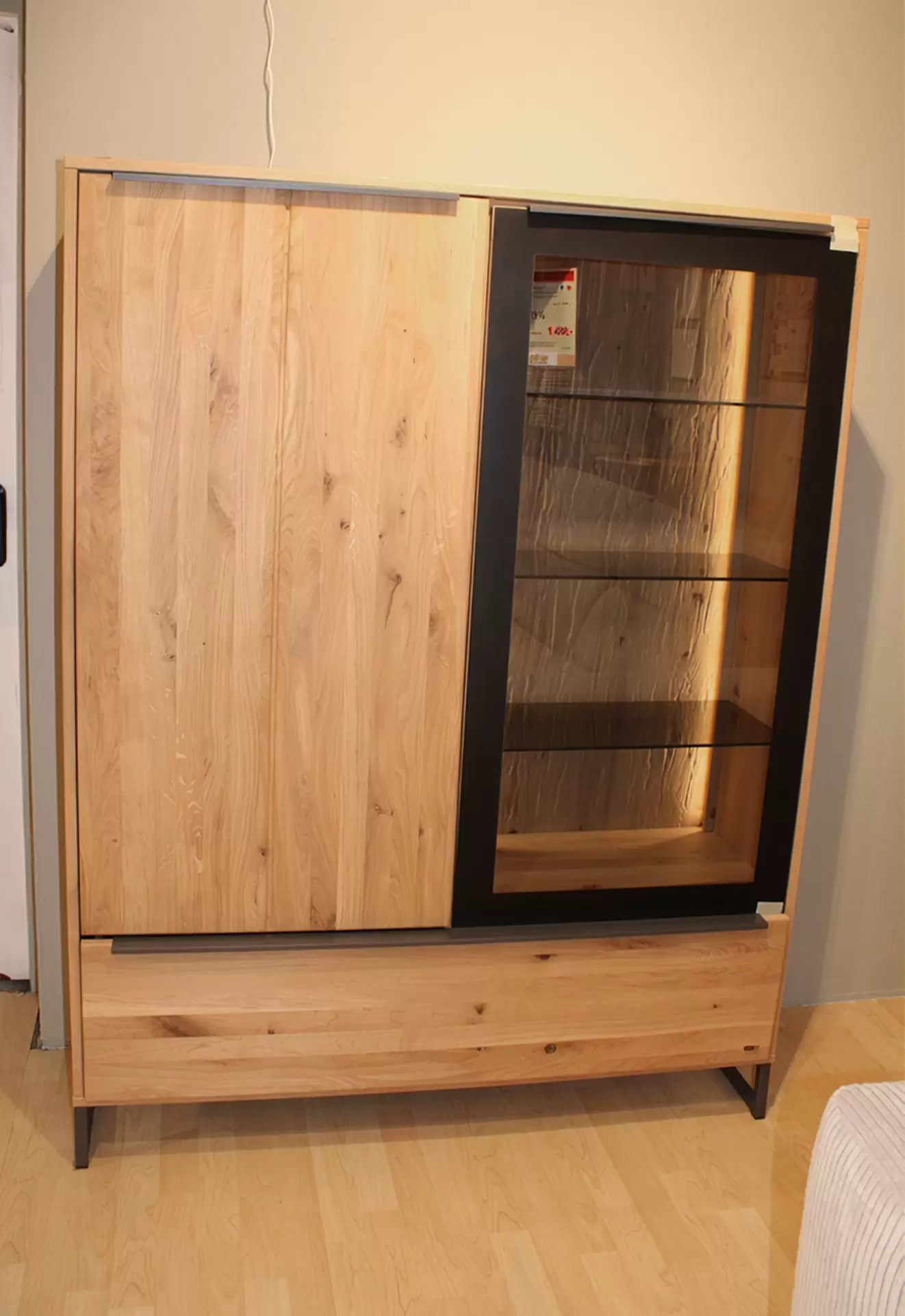 Das Highboard ALAN von Musterring in Eiche Natur mit einer Glastüre und Beleuchtung
