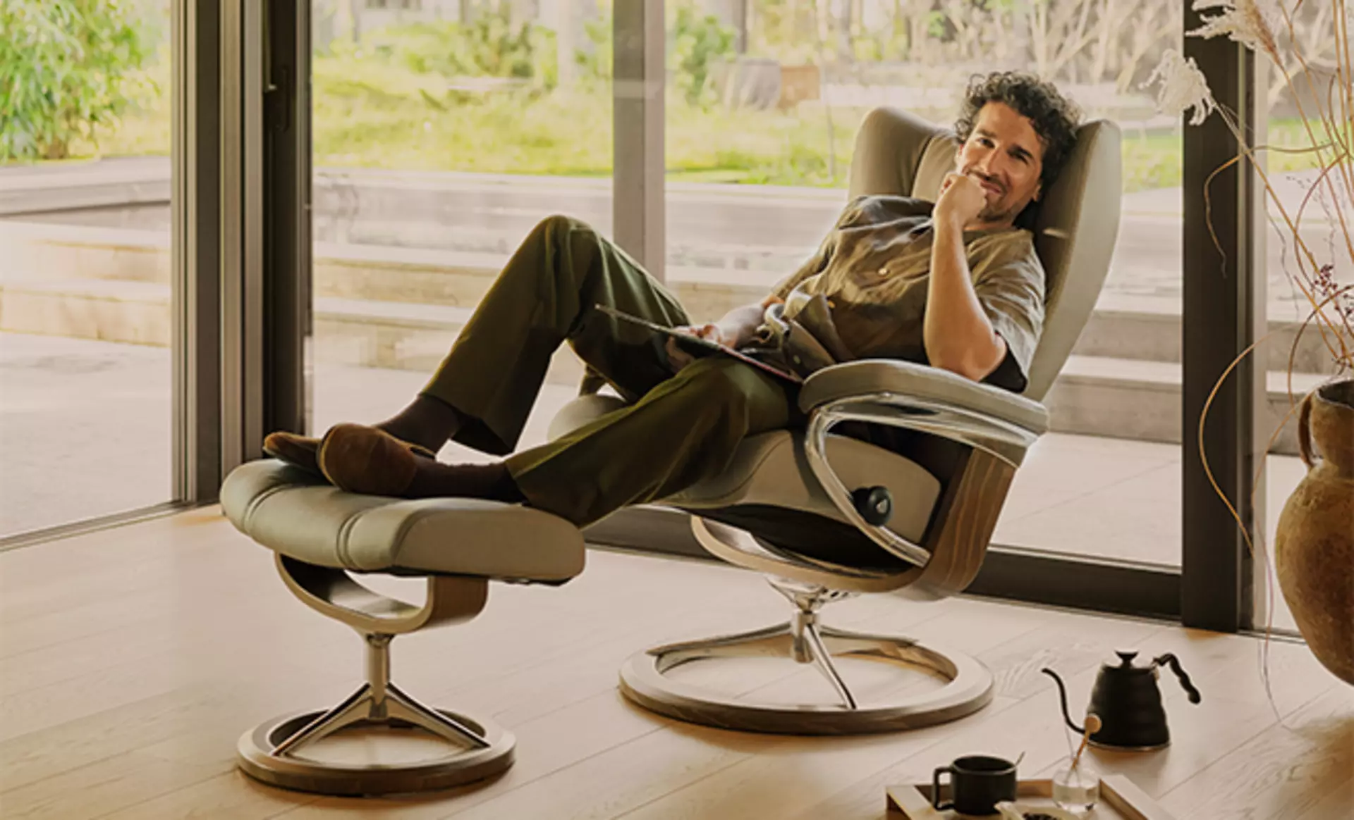 Ein Mann sitzt im Stressless Wing Signature Sessel mit Mushroom Smoked Lederbezug und poliertem Eichengestell 