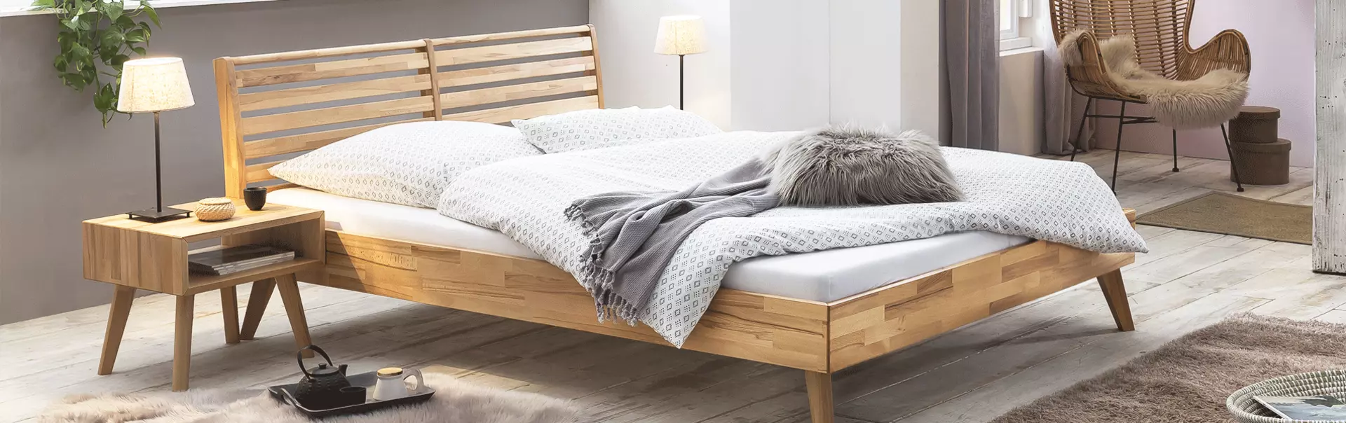 Bett und Nachttisch aus Massivholz. Dazu ein Fellteppich und weiße Bettwäsche.