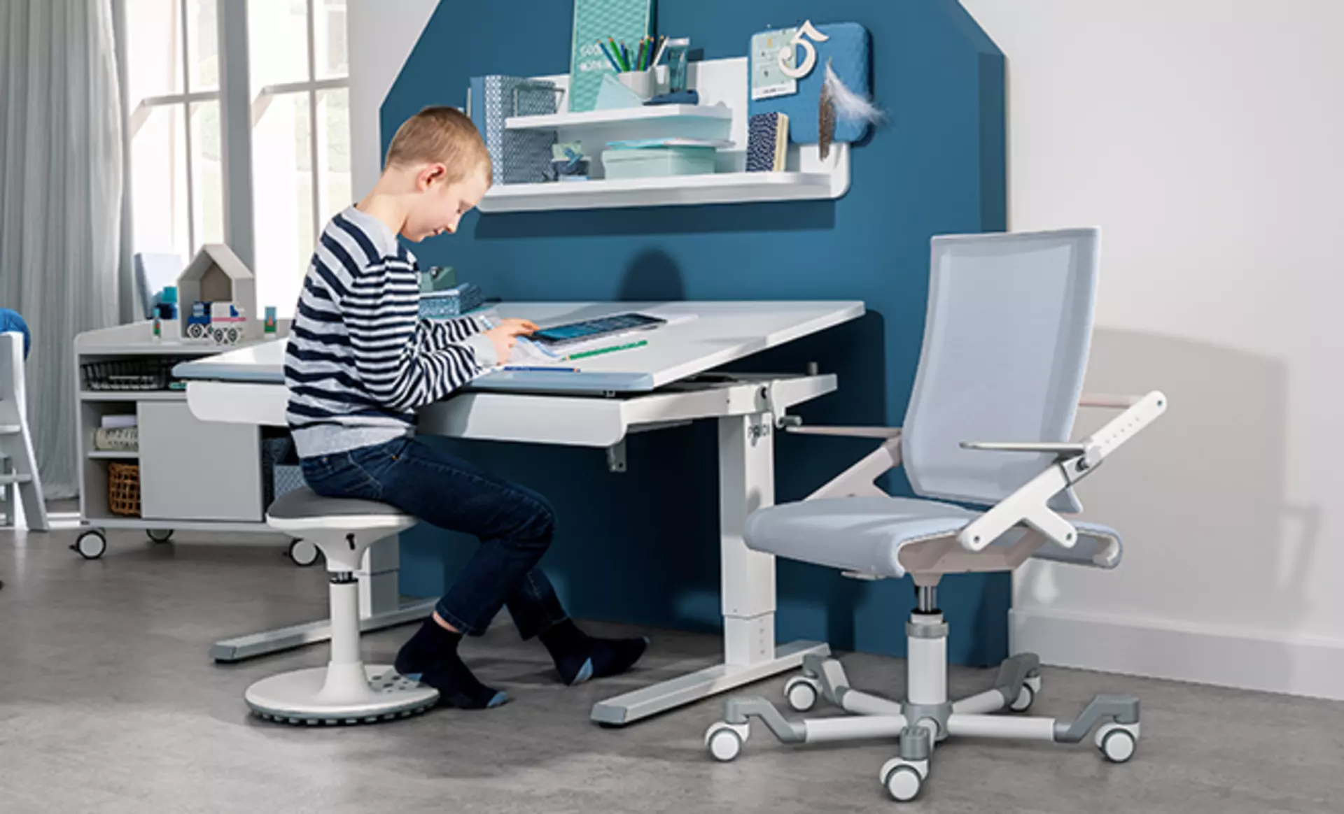 Junge sitzt an Kinderschreibtisch mit geneigter Arbeitsplatte und ergonomischer Sitzhaltung