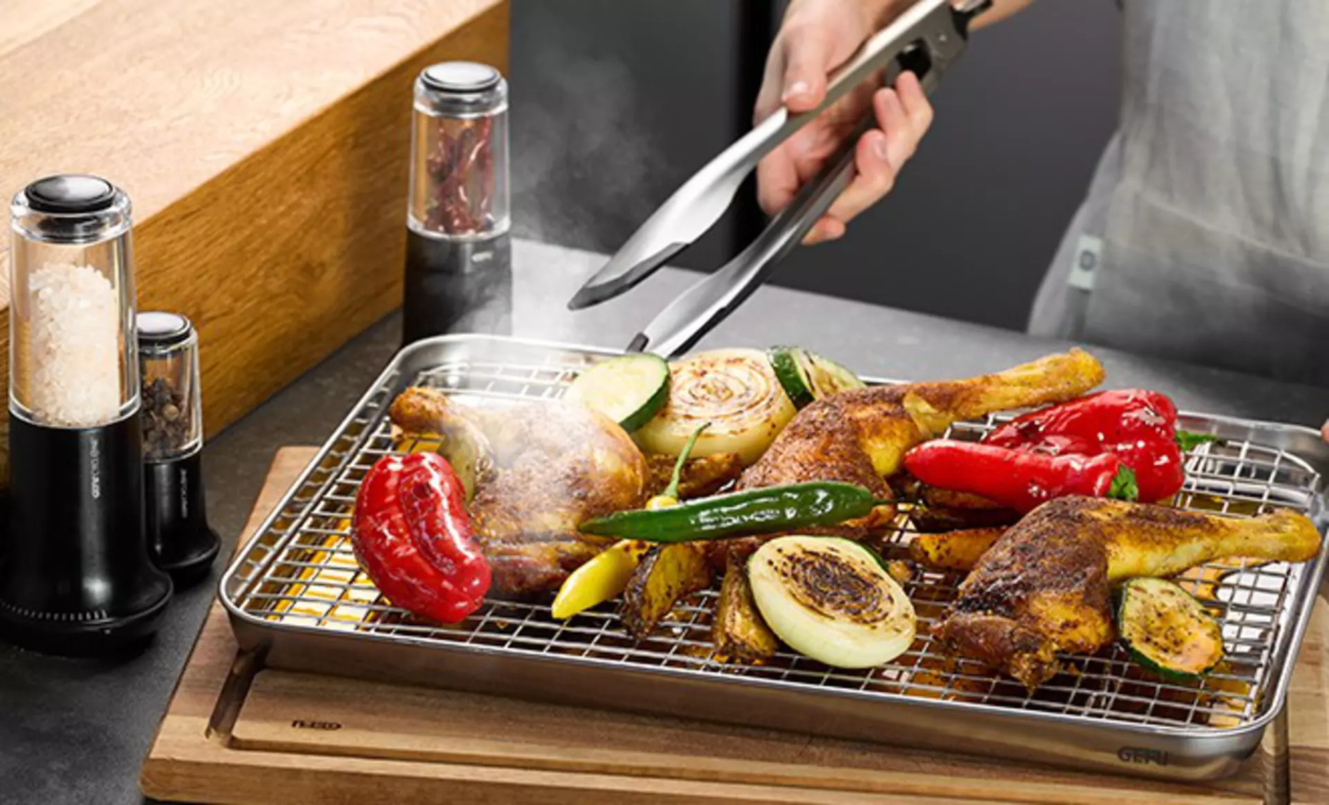 Grillzange mit frisch gegrilltem Gemüse und Fleisch auf einem Grilltablett.