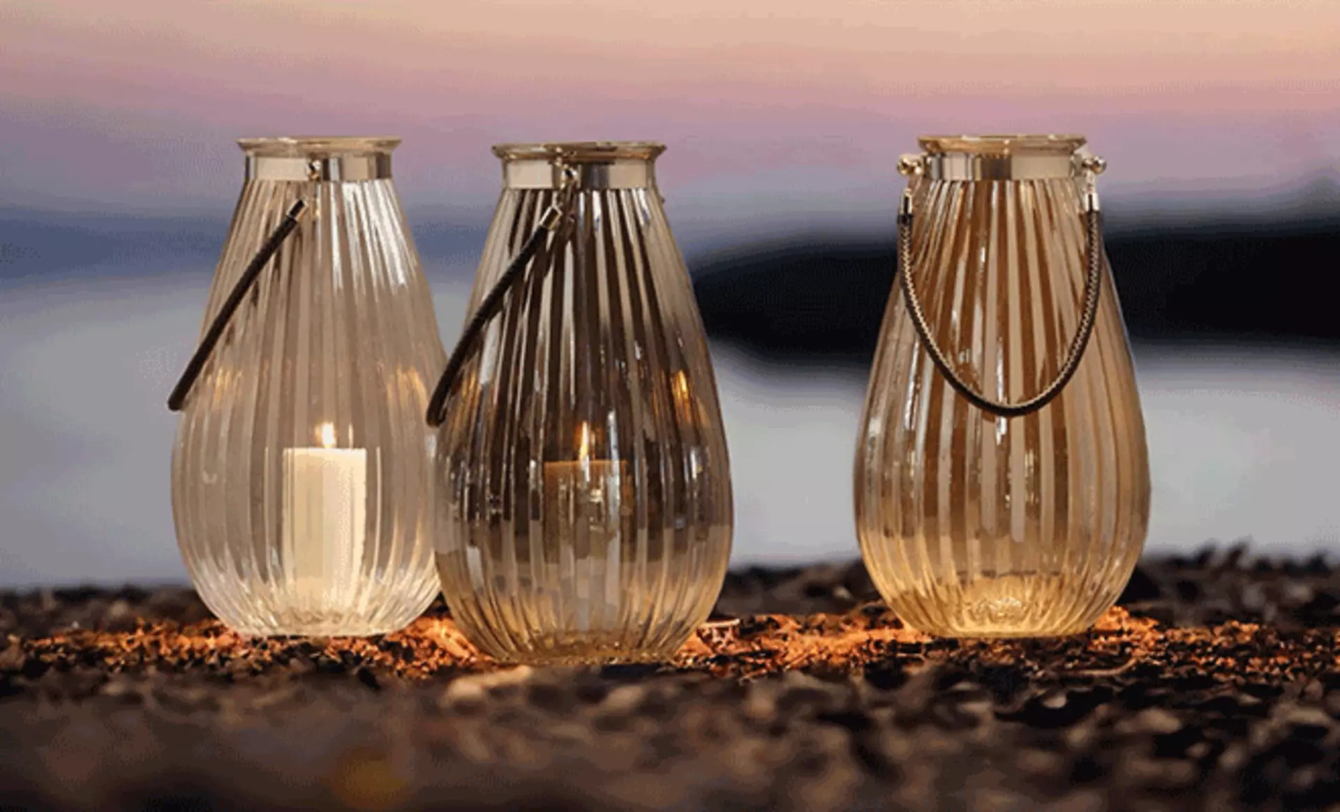 Windlichter auf dem boden wo im Hintergrund ein Meer liegt