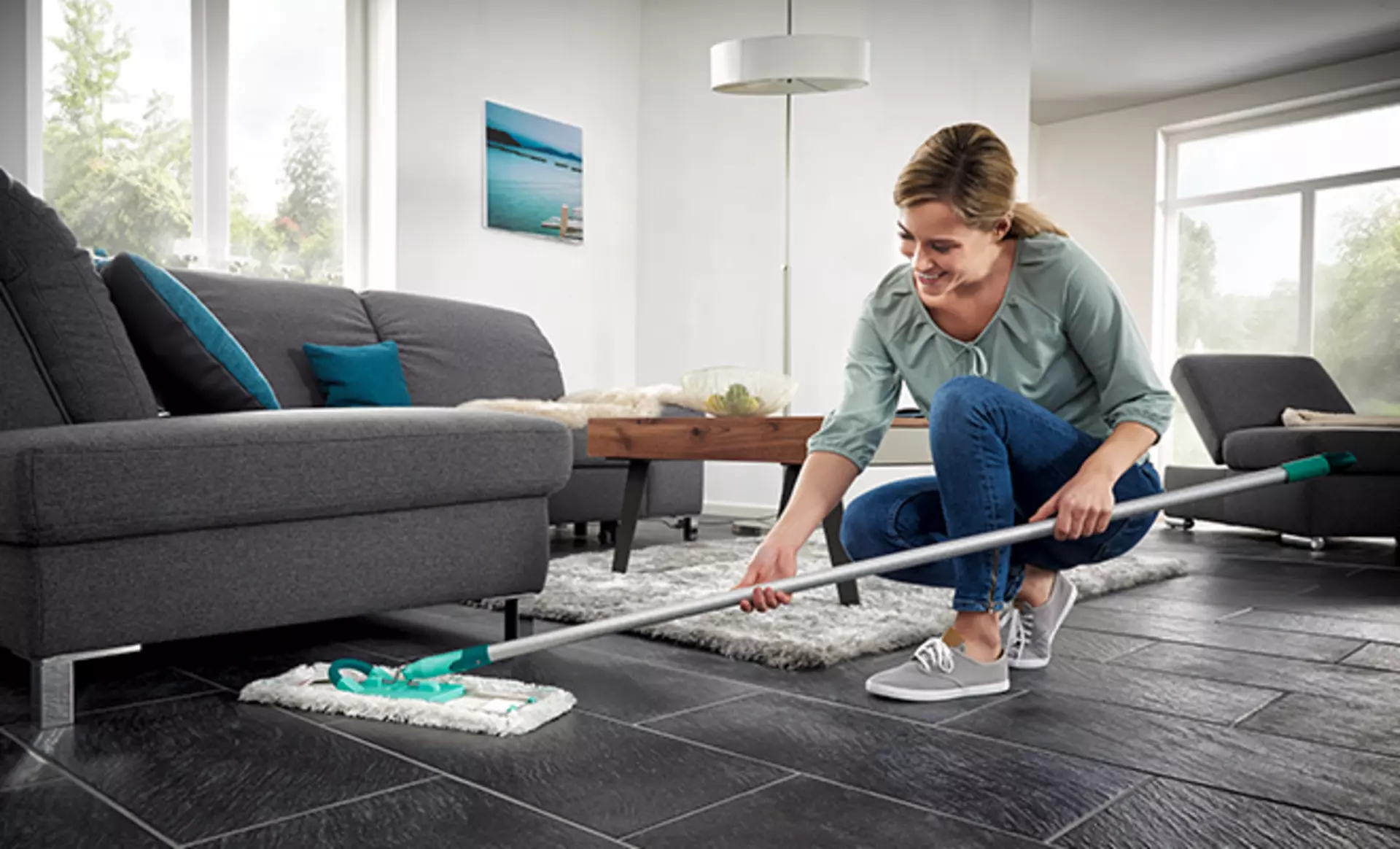 Frau wischt unter einem Sofa mit Leifheit Bodenwischer