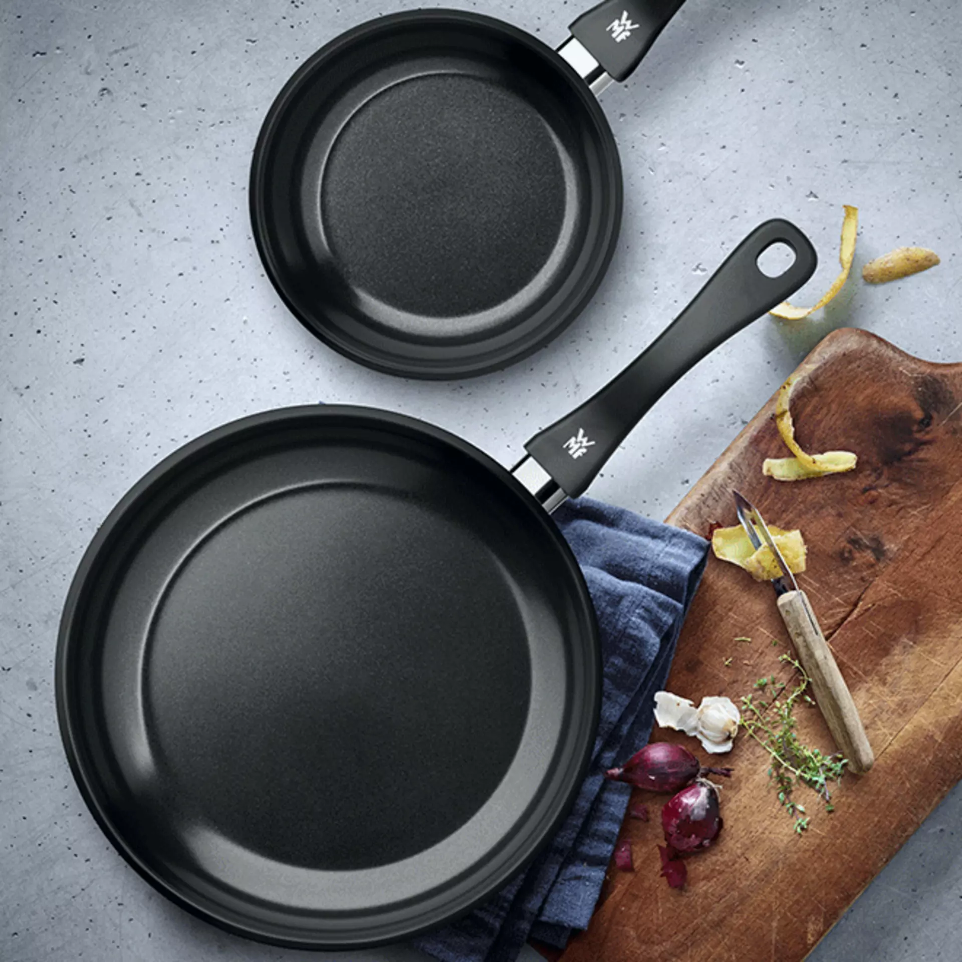2 Pfannen in verschiedenen Größen auf einer Küchenplatte mit einem Schneidebrett