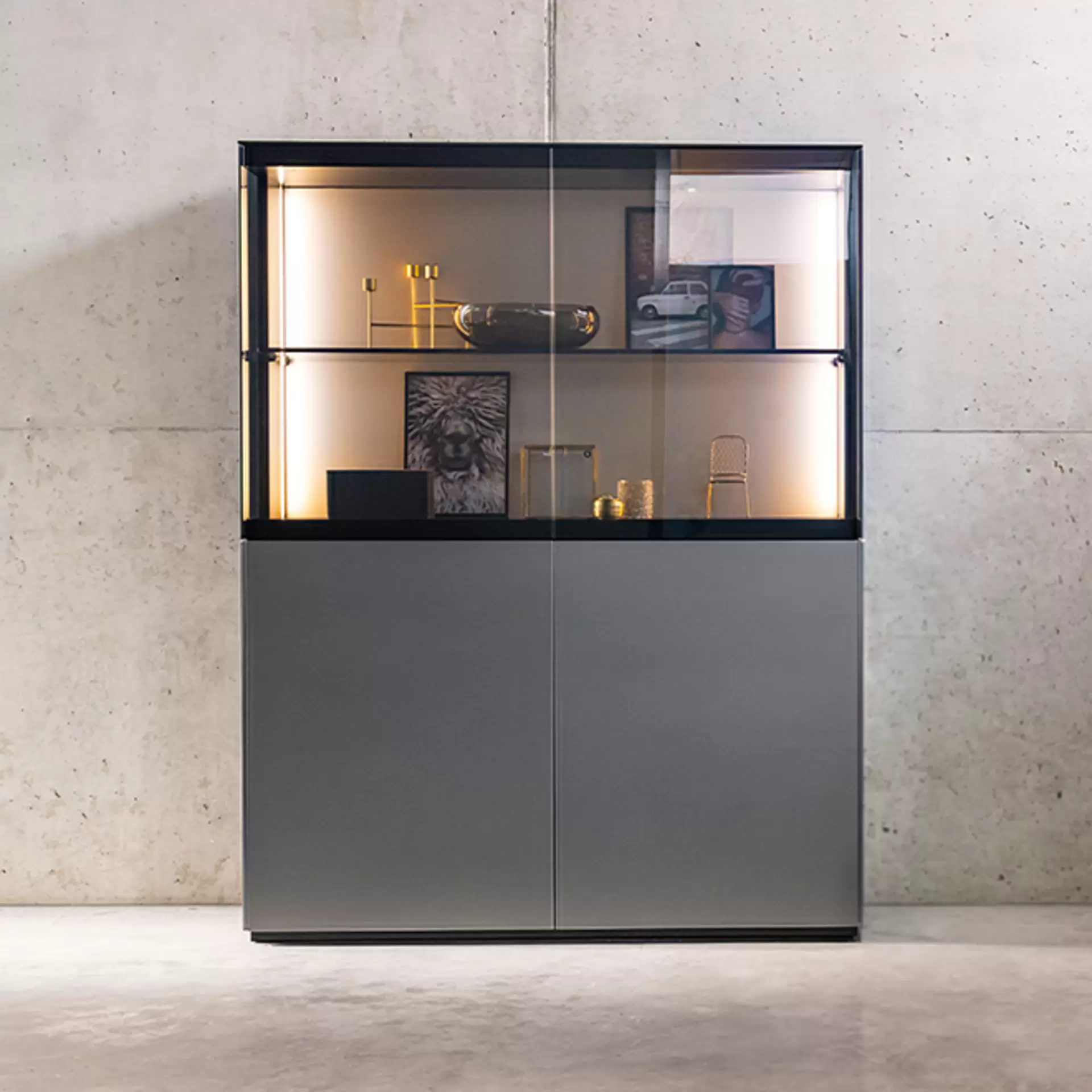 Ein zwei-Flügeliges Highboard von Kettnaker aus der Serie Soma mit halb verglaster front und grauer Lackierung an der unteren Hälfte