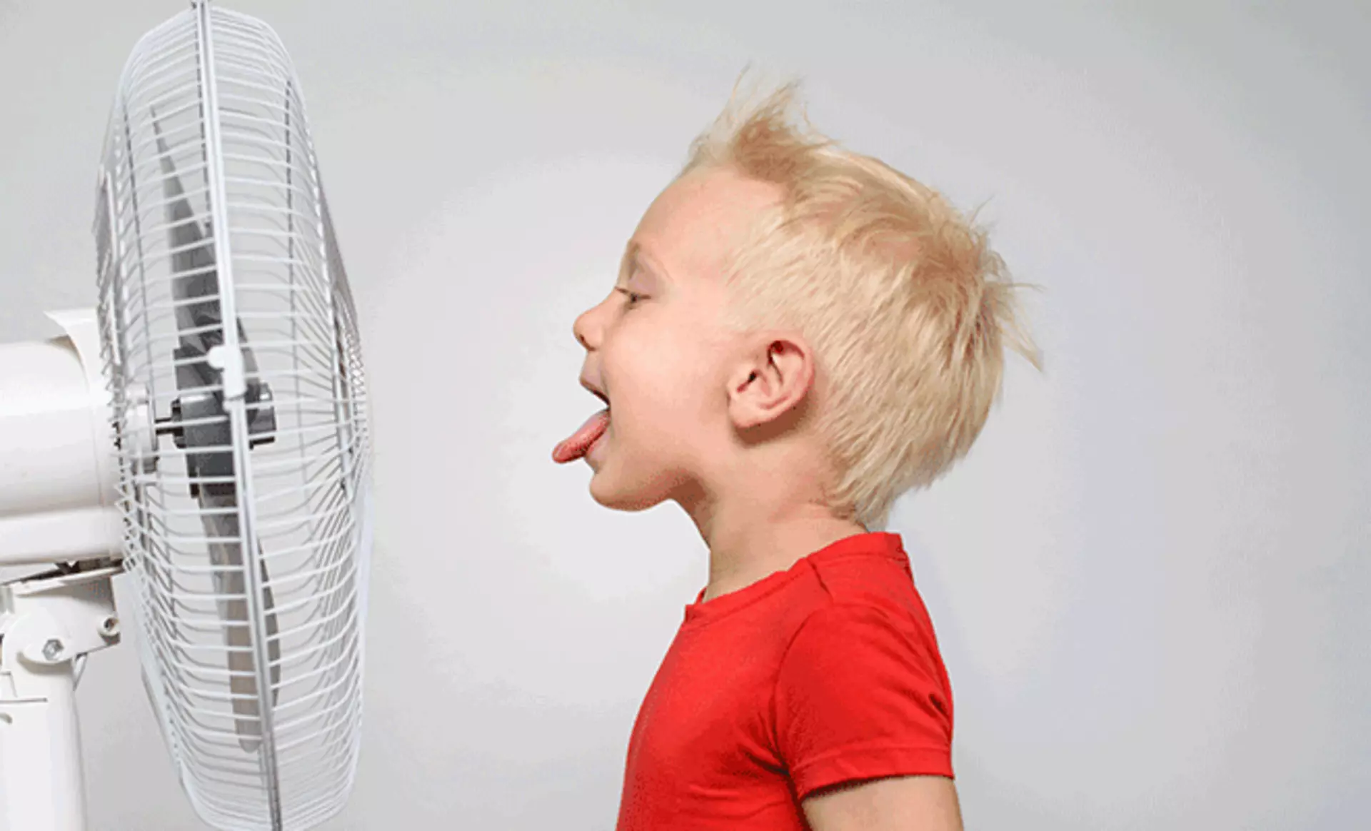 ein kleiner Junge, der seine Zunge herausstreckt, vor einem Ventilator