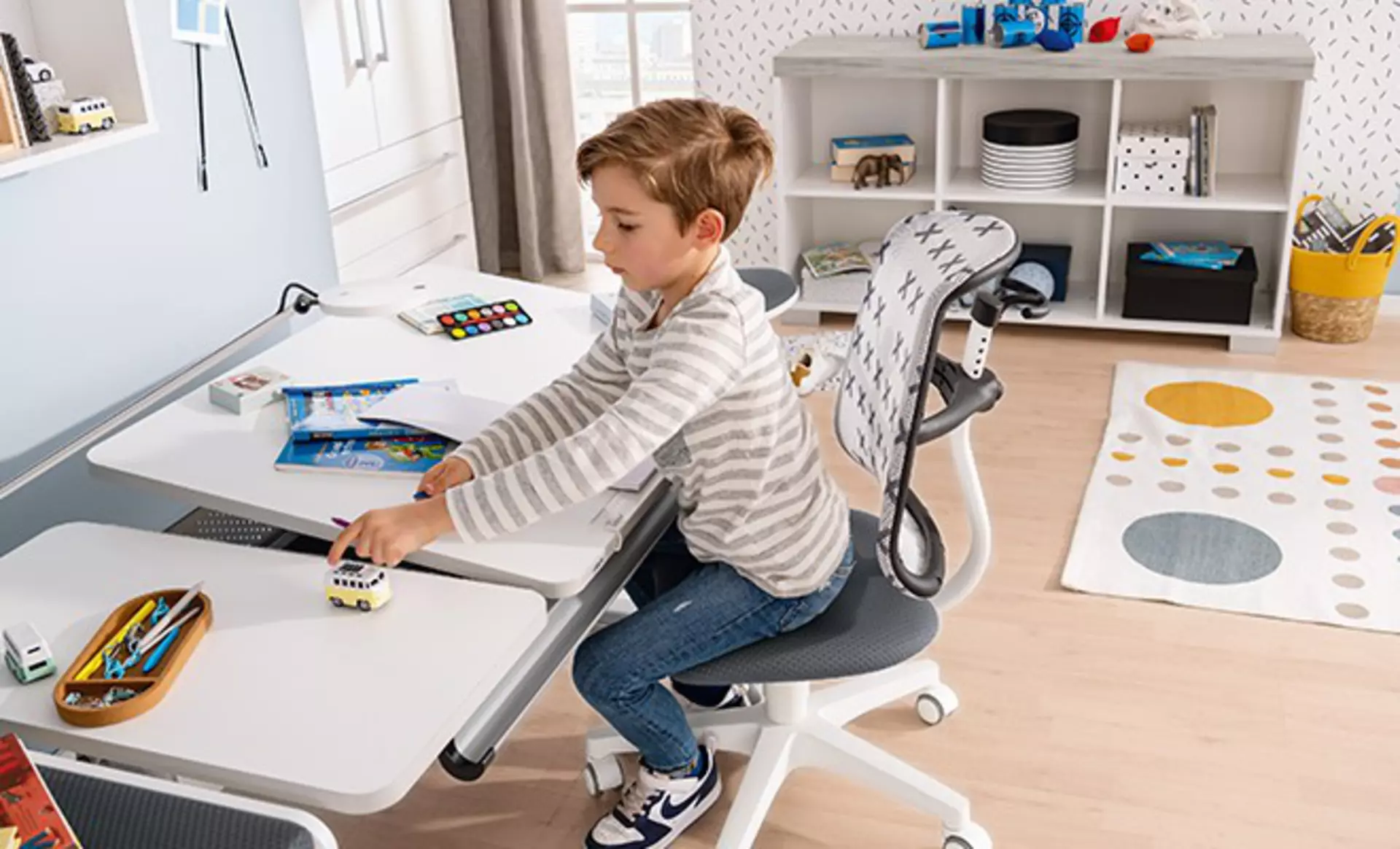 Junge sitzt an einem höhenverstellbaren, ergonomischen Schreibtisch und zeichnet