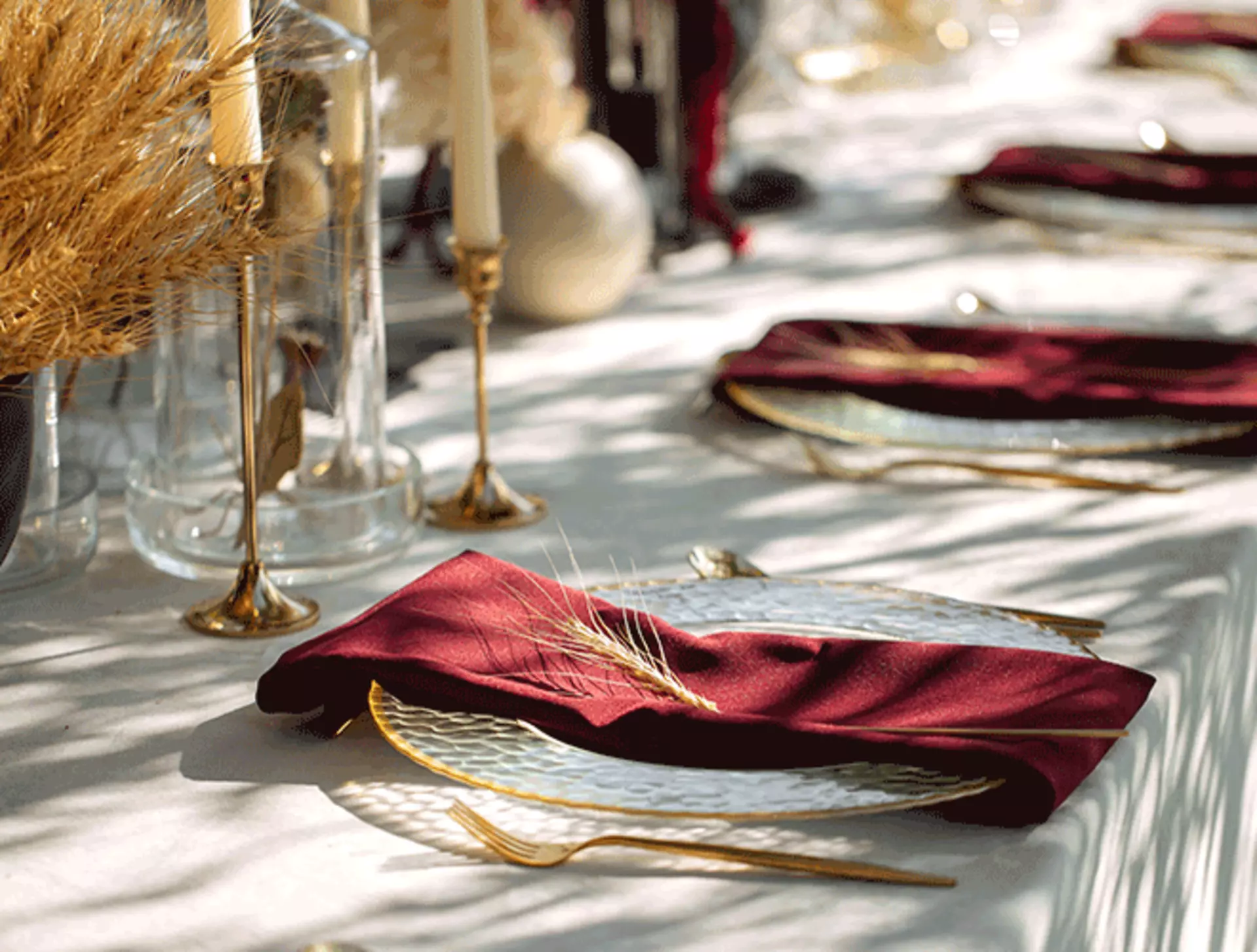 Esstisch mit goldenem Besteck und Kerzenleuchtern, weißen Tellern mit goldenen Akzenten und roten Servietten.