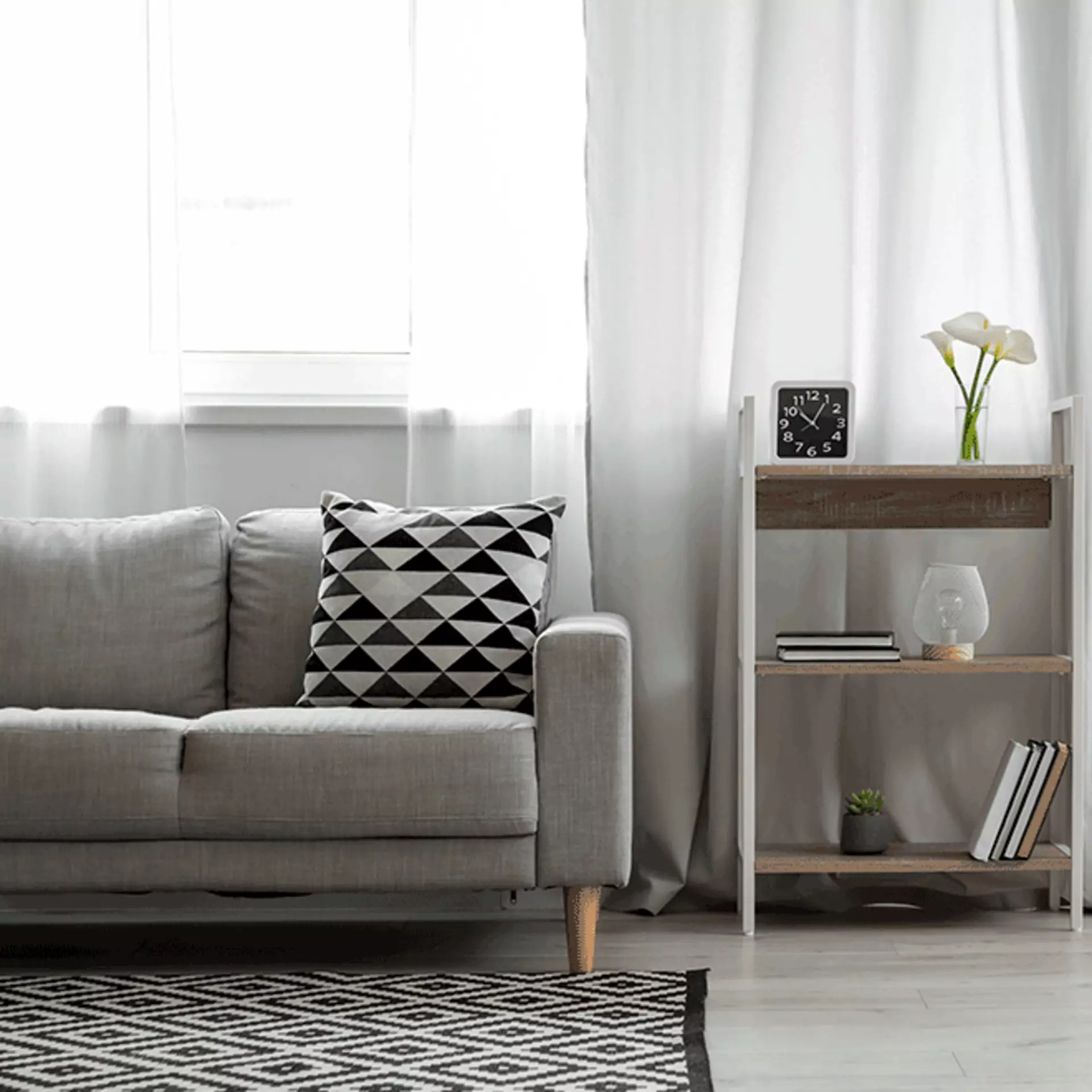 Ein hellgraues Sofa und ein weißes Regal, dekoriert mit kleinen Topfpflanzen und schwarzen und weißen Akzenten.