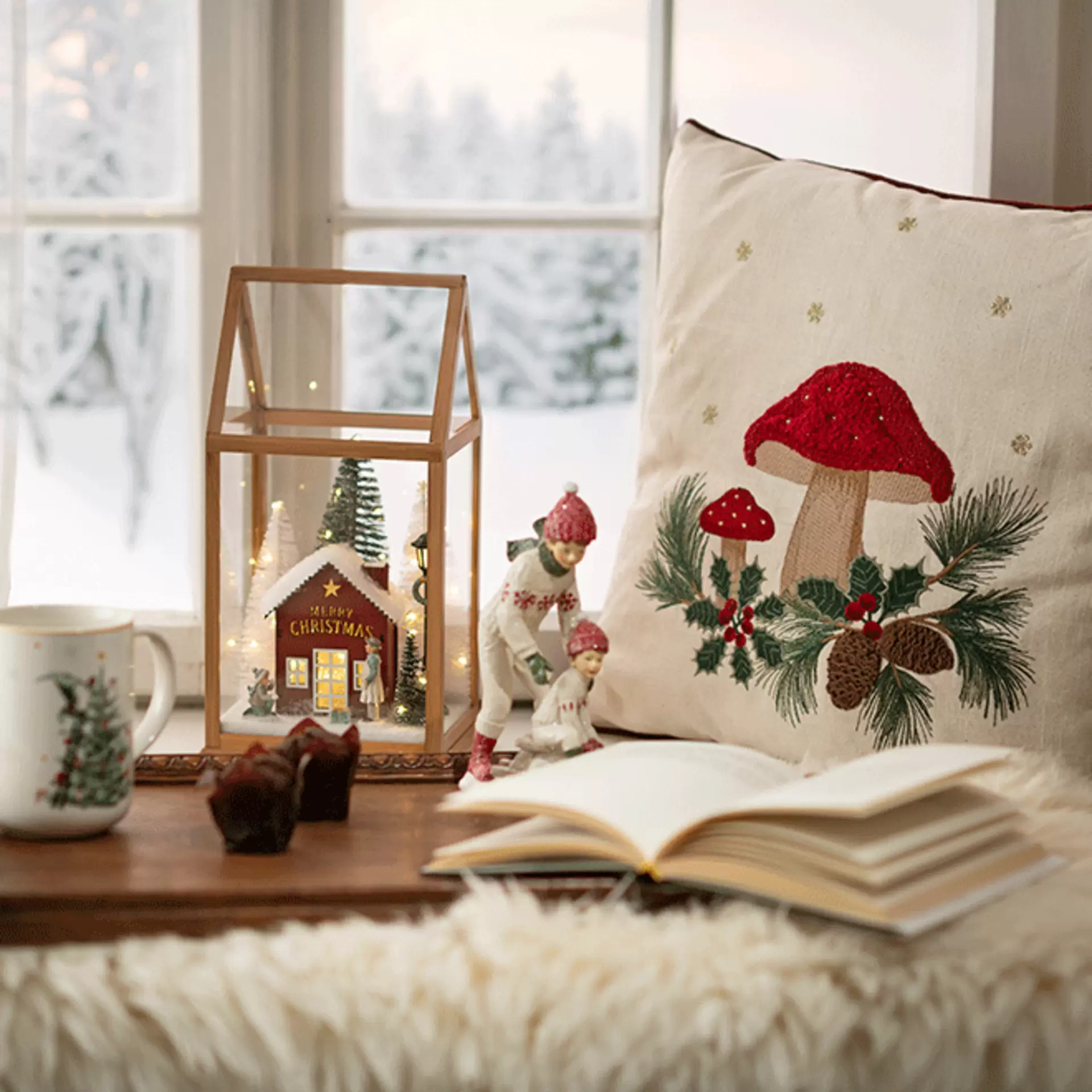 Skandi-Weihnachtsdokoration am Fenster mit beleuchtetem Holzhaus und gemütlichen Kissen