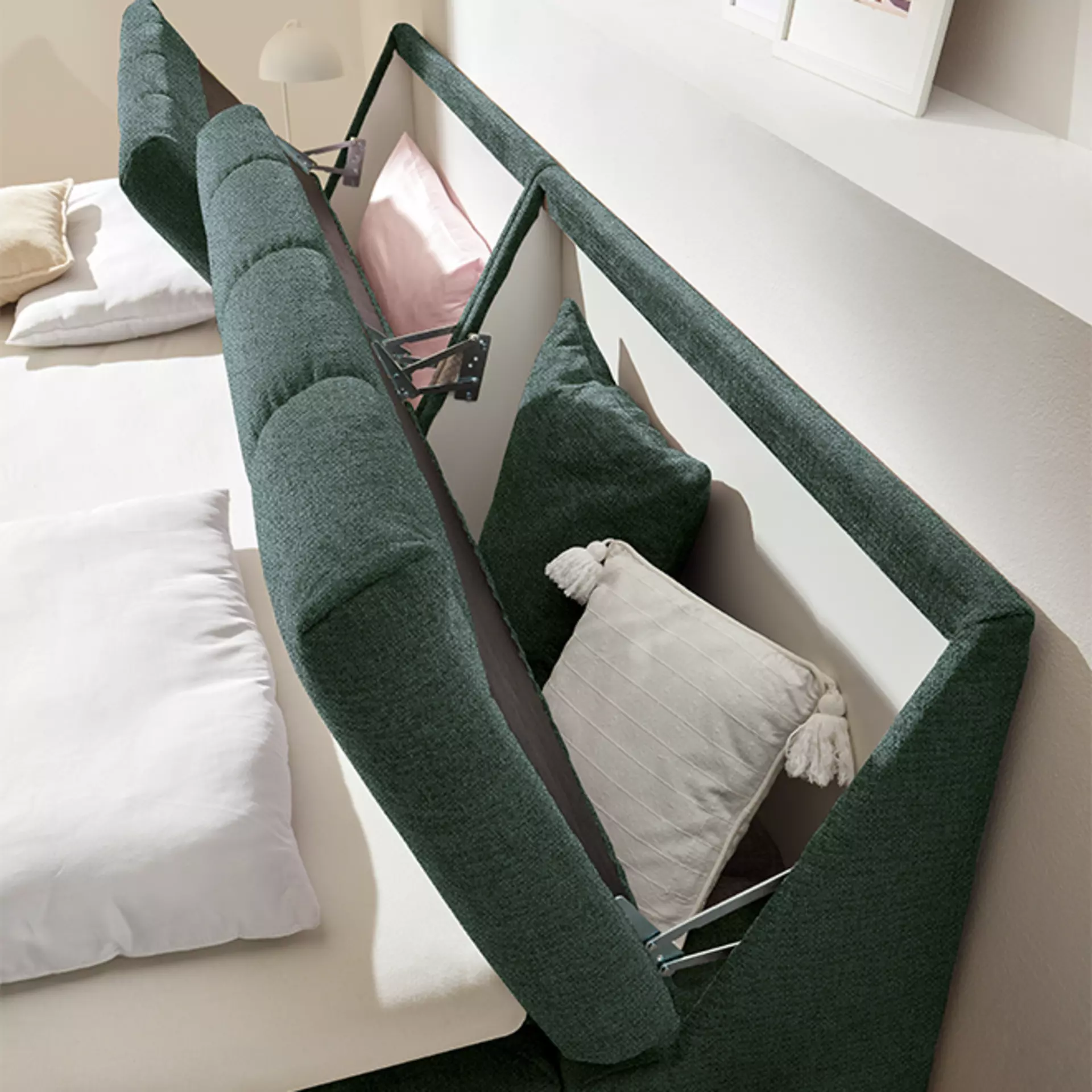 Boxspringbett in samt grünem Stoffbezug. Das Kopfteil bietet Stauraumfächer für Dekokissen