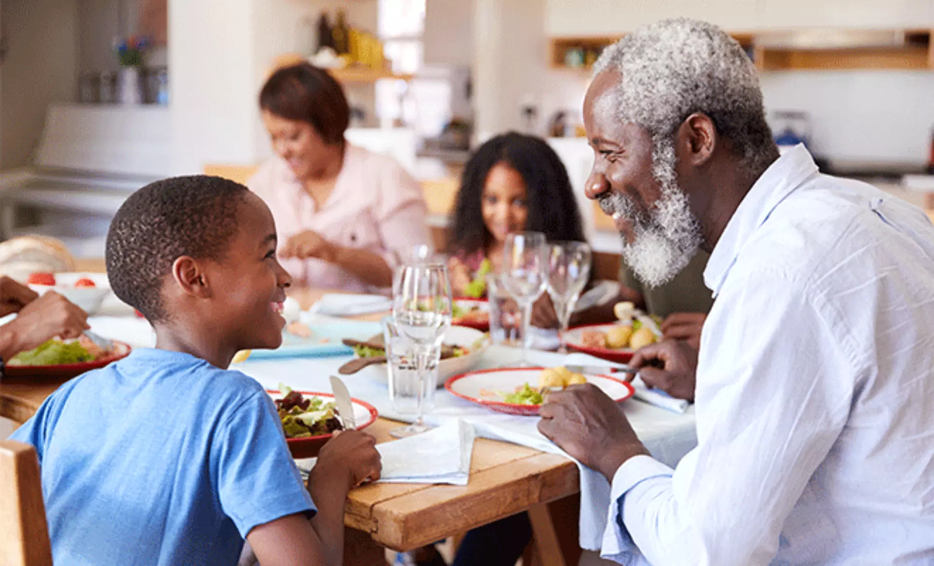 Eine Mehrgenerationenfamilie sitzt fröhlich zusammen am Esstisch und genießt gemeinsam das Abendessen.