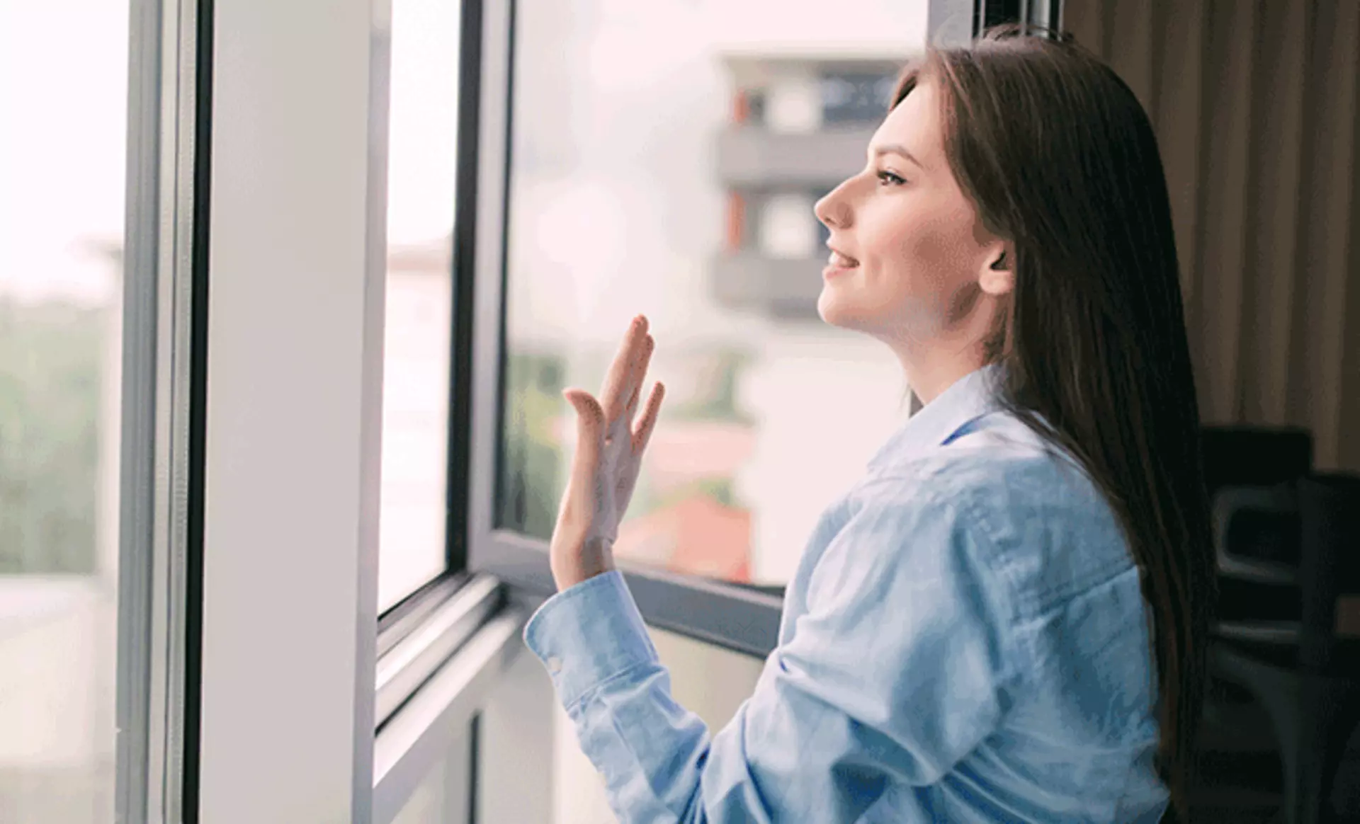 eine Frau, die durch das Fenster frische Luft hereinlässt 