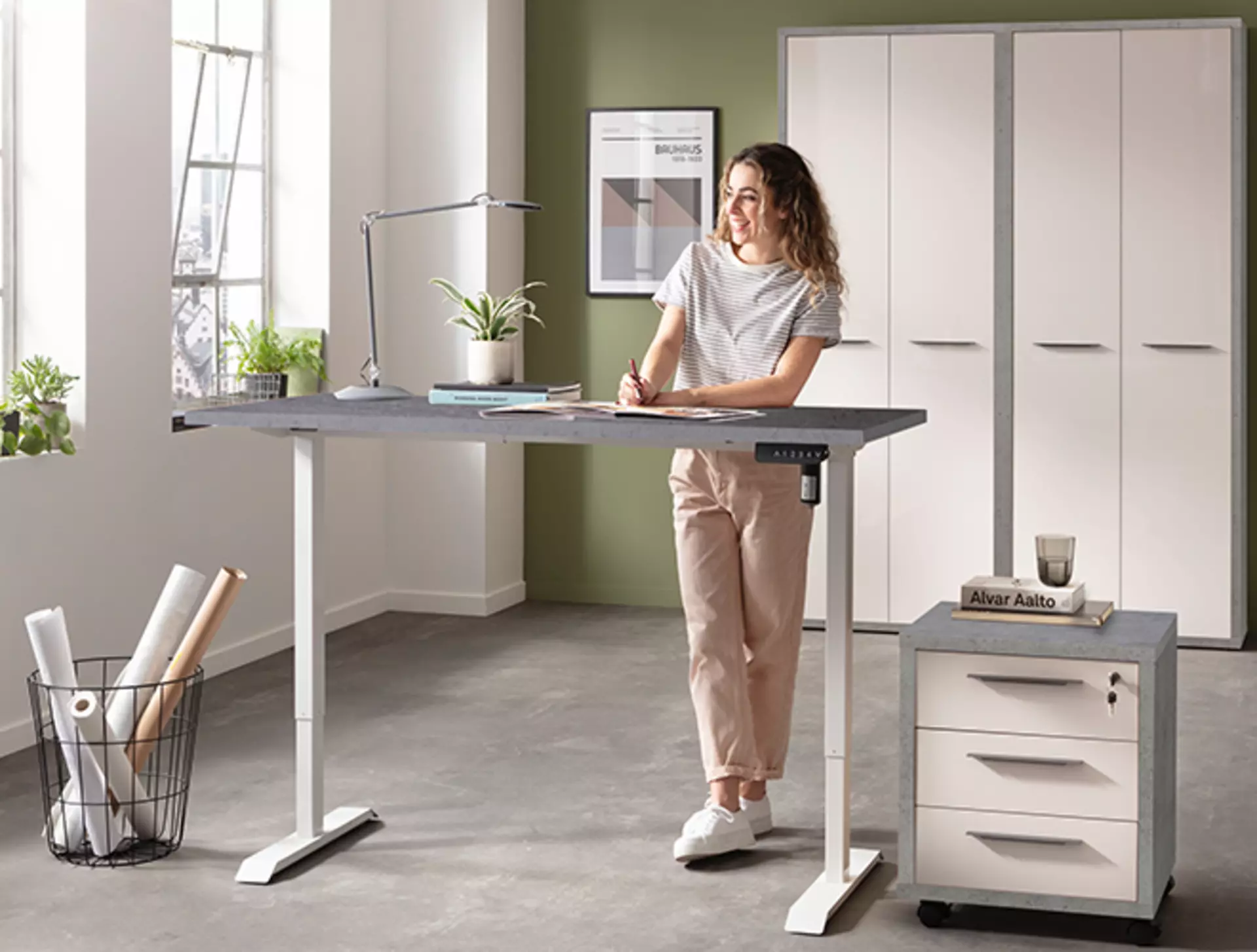 Frau steht an Stehschreibtisch in hellem Arbeitszimmer mit grauen Rahmenfurnieren