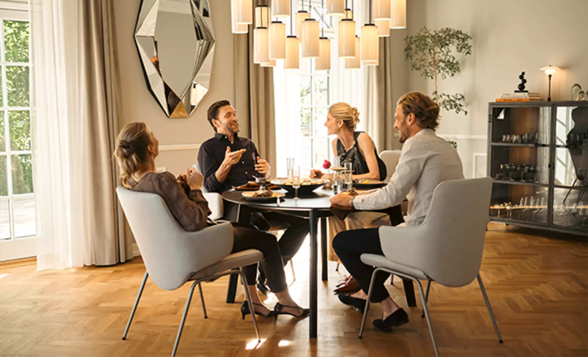 Freunde sitzen gemeinsam beim Abendessen auf Stressless Esszimmerstühlen an einem runden Tisch im skandinavischen Design