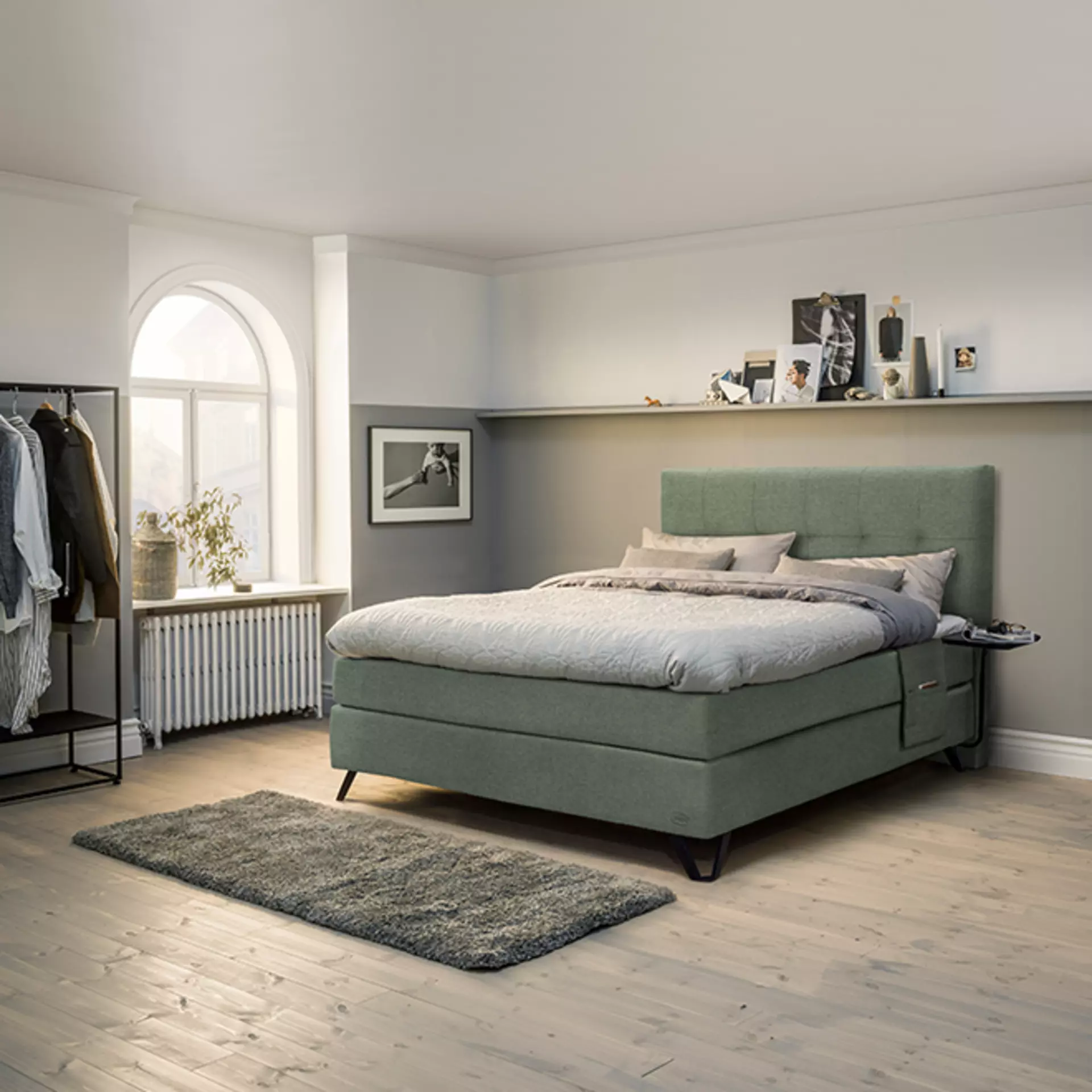 Das Jensen Diplimat Continental Boxspringbett in Pastellgrün in einem schick eingerichteten Schlafzimmer mit Kleiderständer und Wandregalen