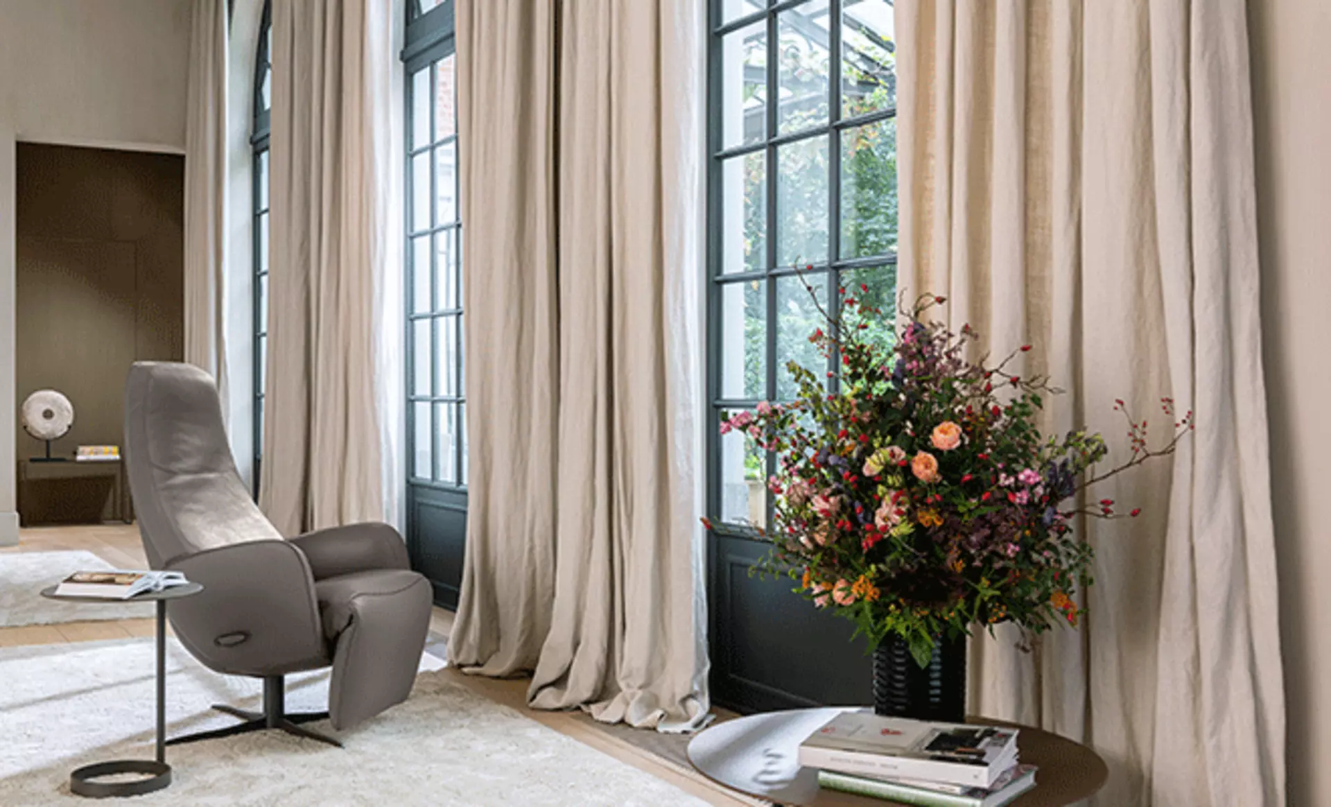 Fensterfront mit hellen Vorhängen, vor welchen ein Relaxsessel steht