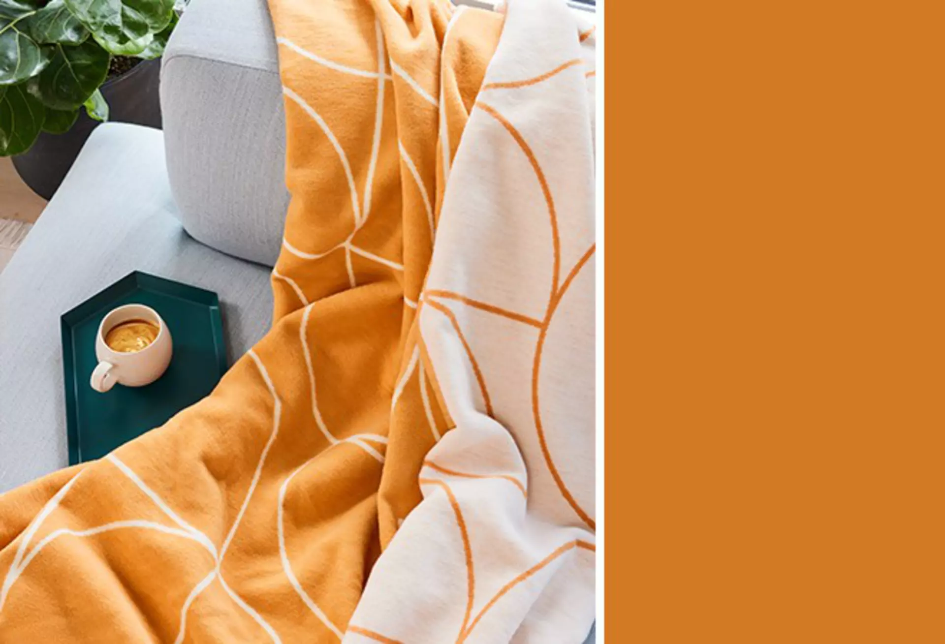 Nahaufnahme einer orange-cremefarbenen Decke auf grauem Sofa.