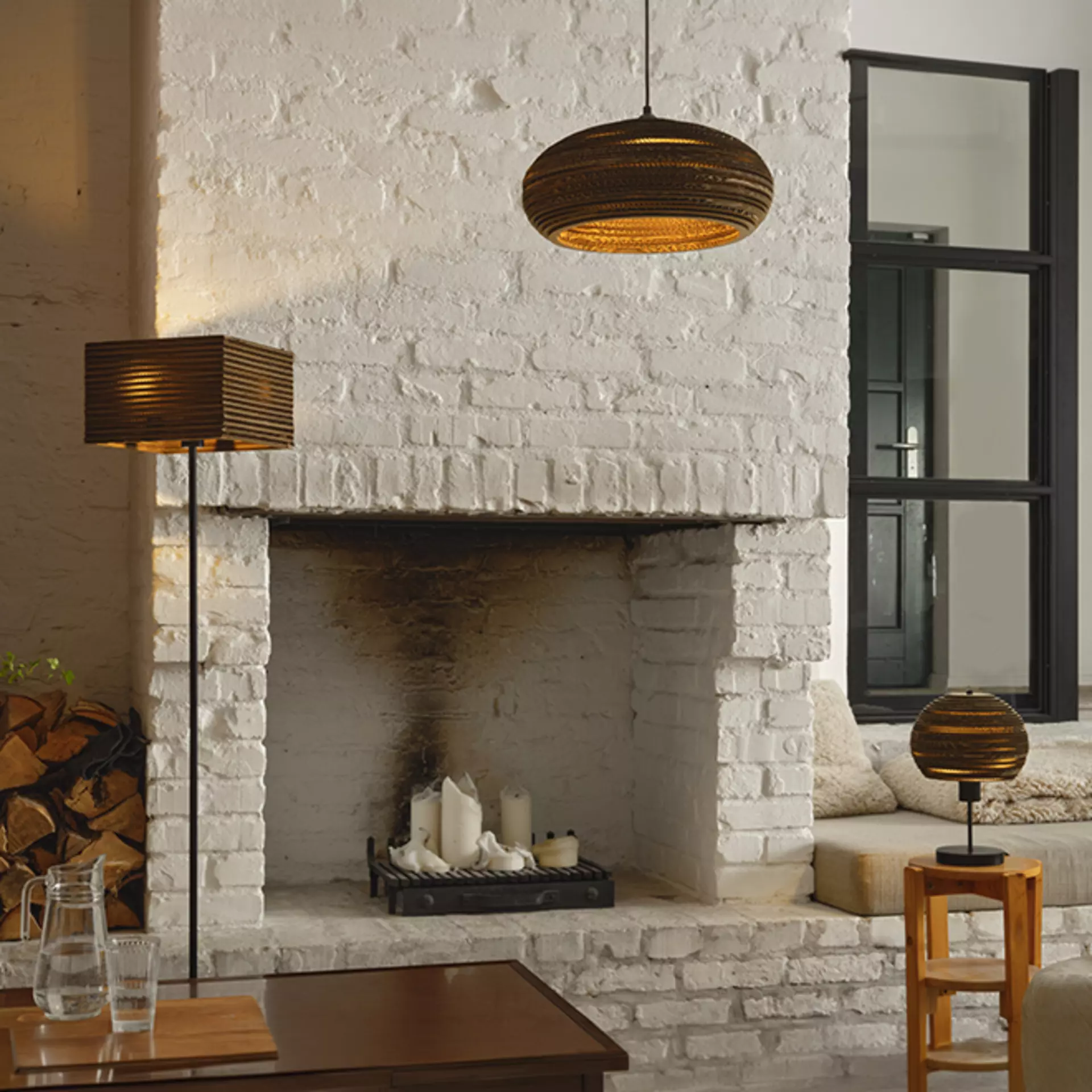 Die Cardboard-Ball Kollektion von Osram mit seiner Pendelleuchte, Stehleuchte und Tischleuchte in einem steinenen Wohnzimmer. mit Kamin