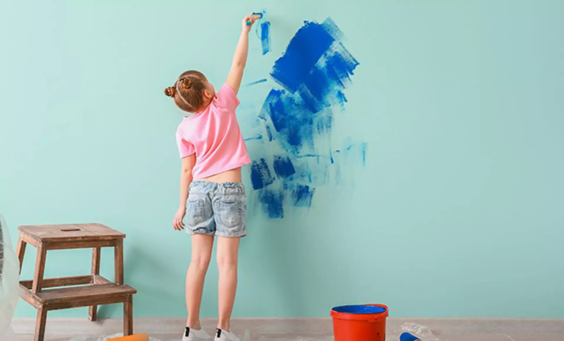 Kind streicht eine Wand im Kinderzimmer blau.