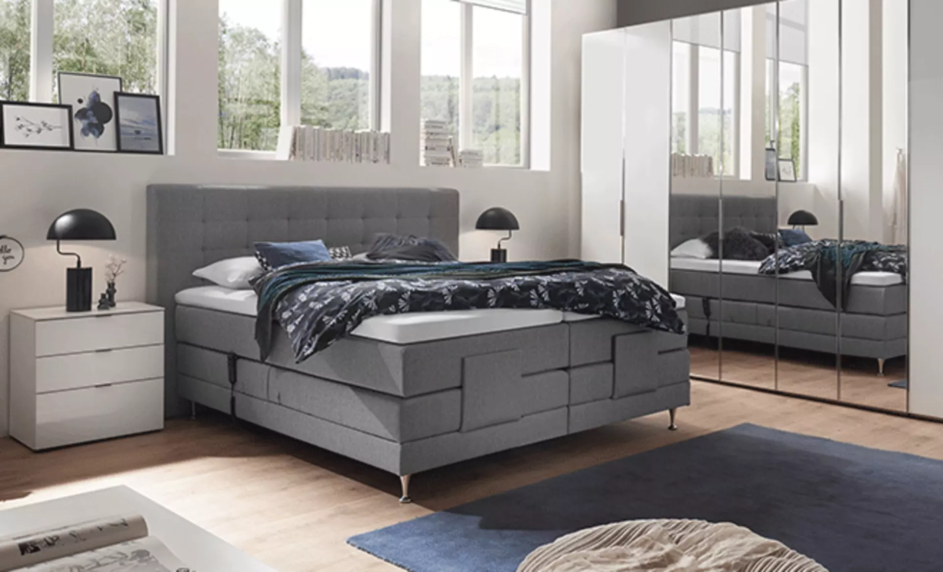 Hell dekoriertes Schlafzimmer mit grauem Bett und Spiegelschrank