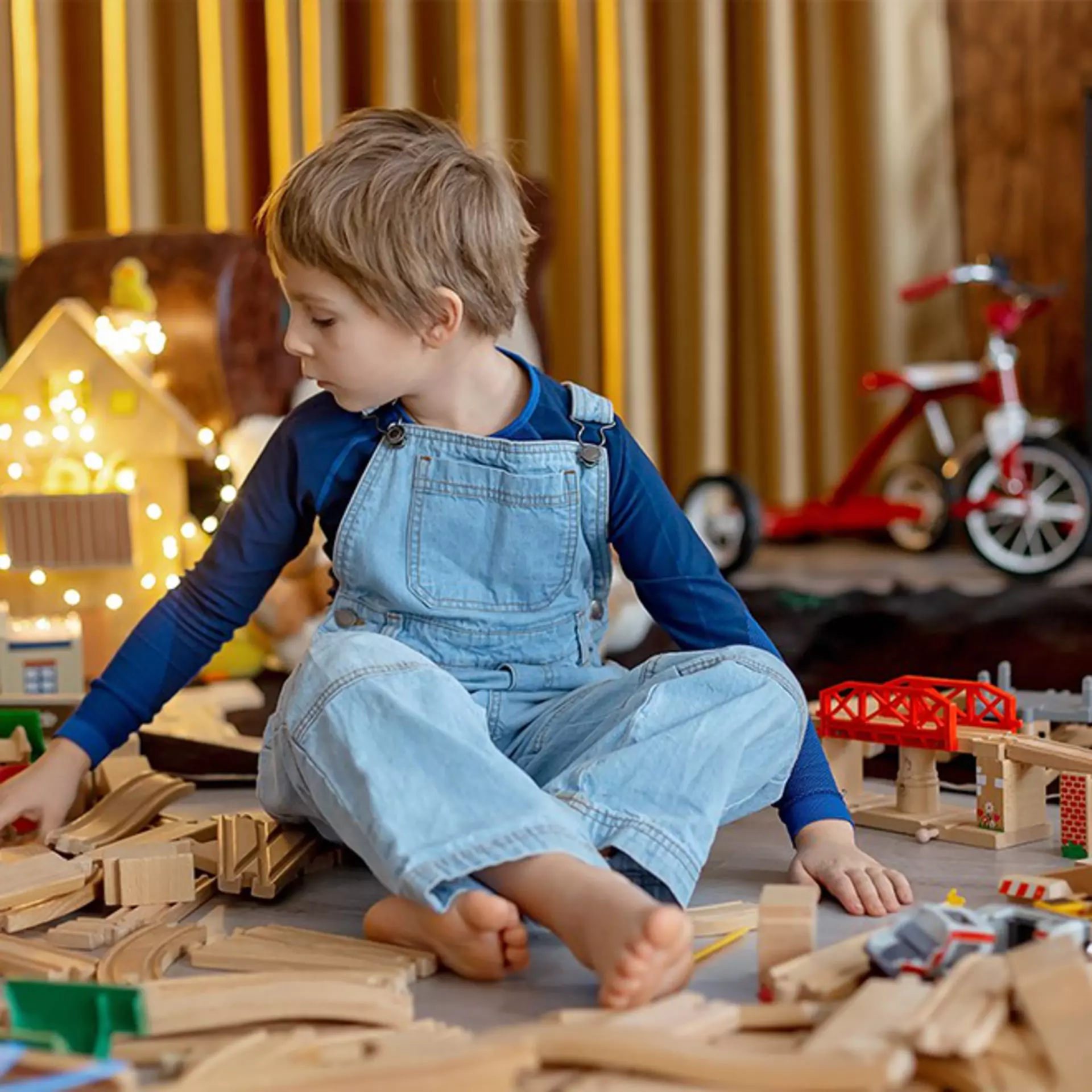 Kind sitzt auf dem Boden umgeben von vielen Spielsachen.